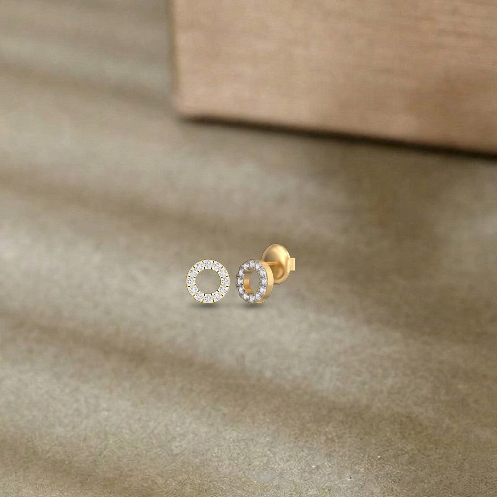 Gold and diamond round-shaped stud earring on a beige surface