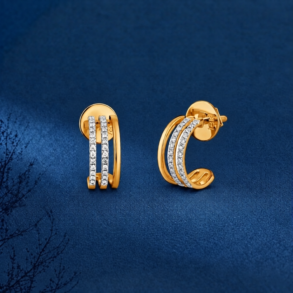 A pair of gold hoop earrings with three parallel rows of small clear stones on the front, displayed on a textured dark blue background.