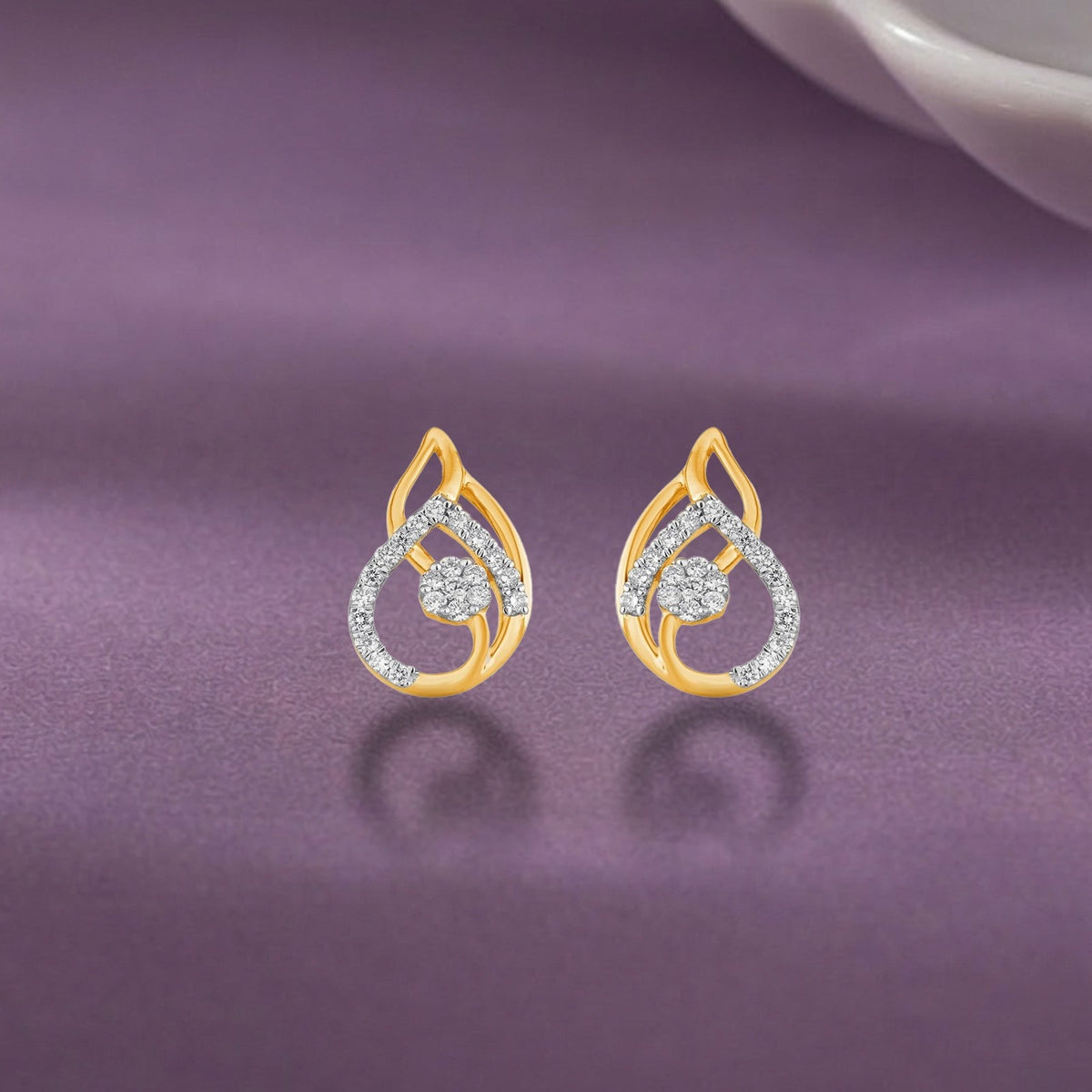 A pair of gold teardrop-shaped stud earrings, displayed on a purple satin surface with a soft reflection.