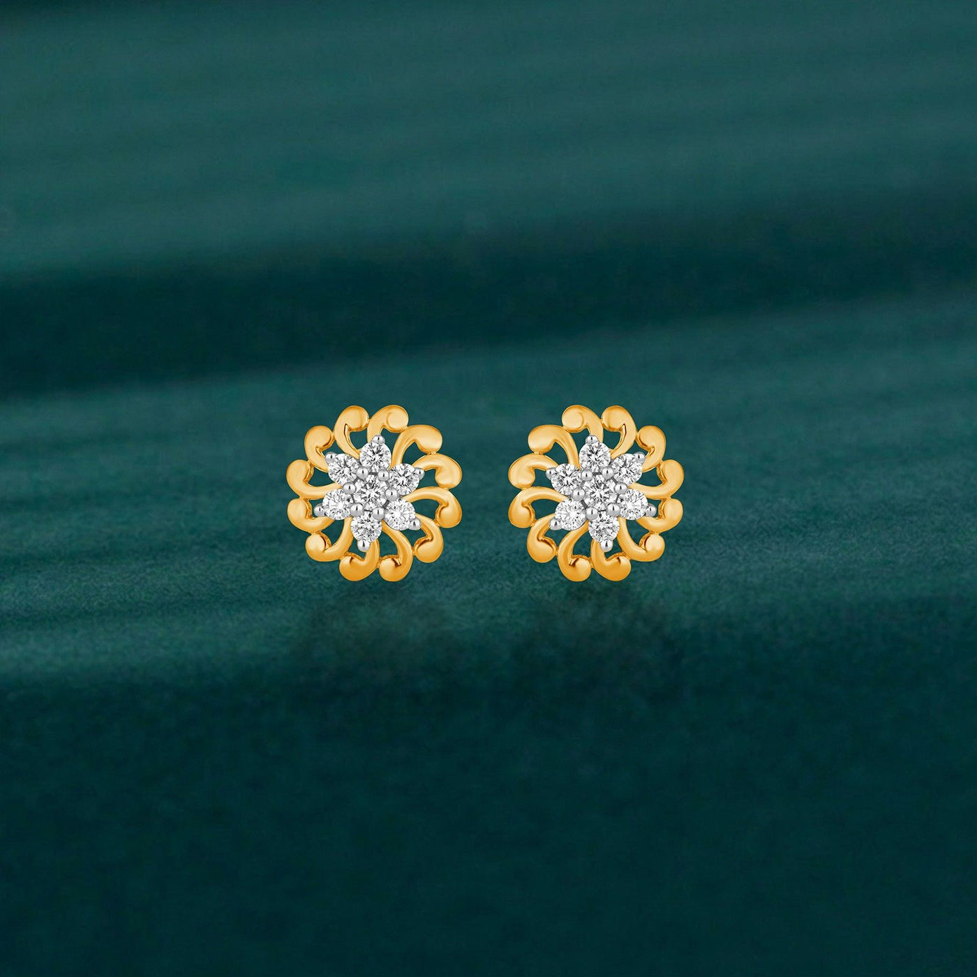 A pair of gold flower-shaped stud earrings with clear crystal centers, displayed on a dark teal textured background.