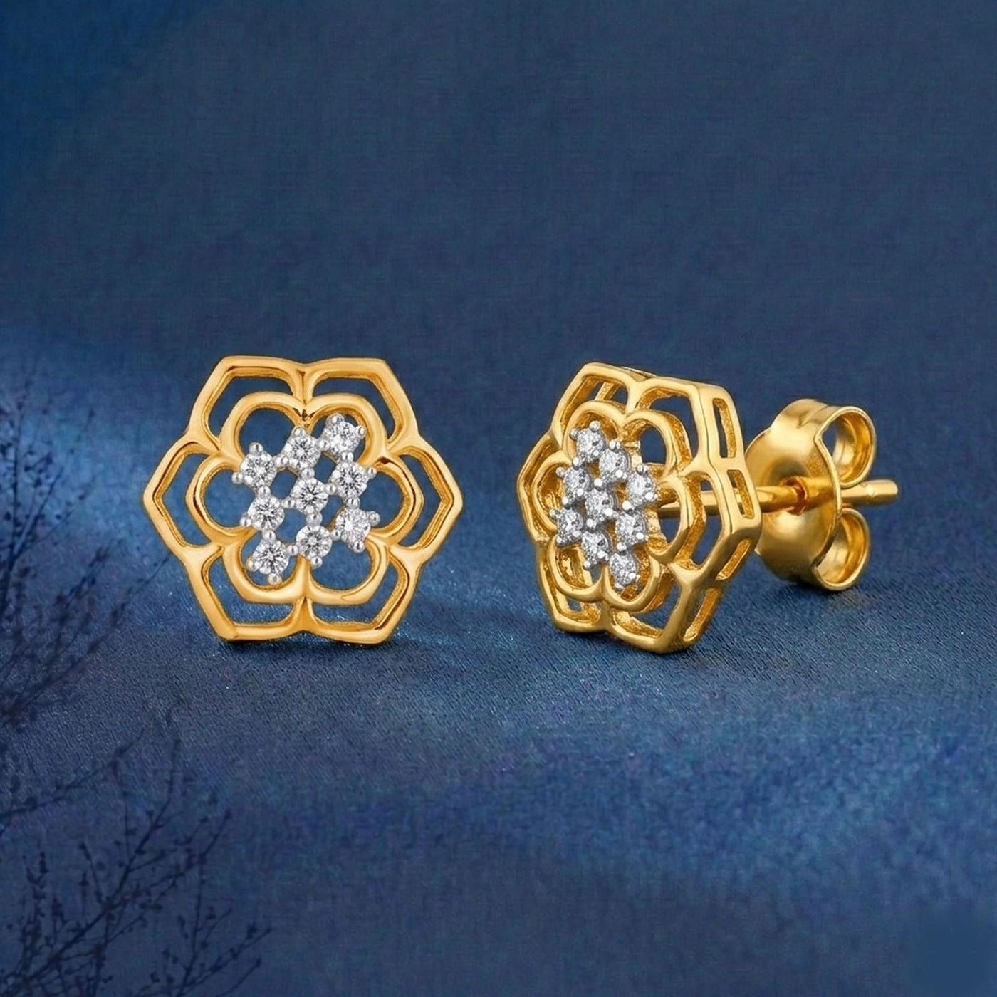 A pair of gold and diamond floral design stud earrings, displayed on a textured dark blue background.
