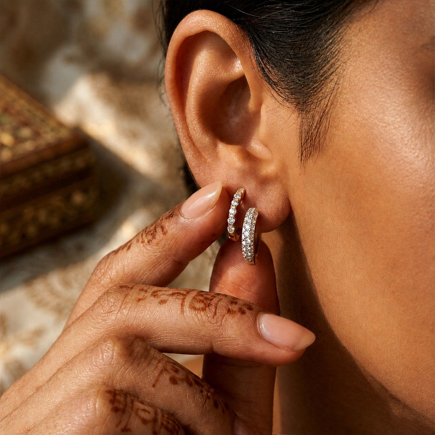 A close-up lifestyle shot of a person wearing a pair of diamond huggie hoop earrings.