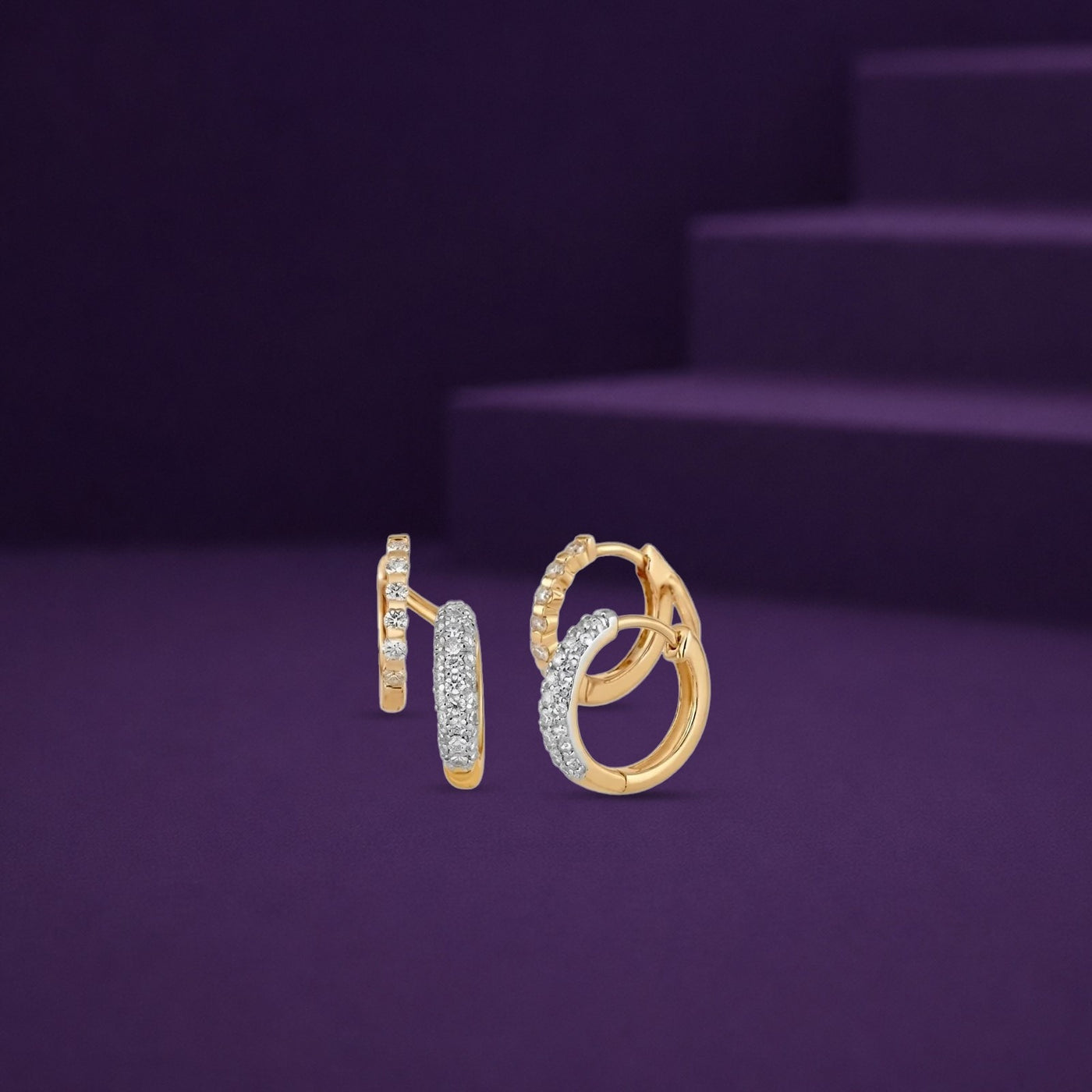 A pair of gold hoop earrings with pavé-set clear stones, shown on a dark purple background with a matching display stand.