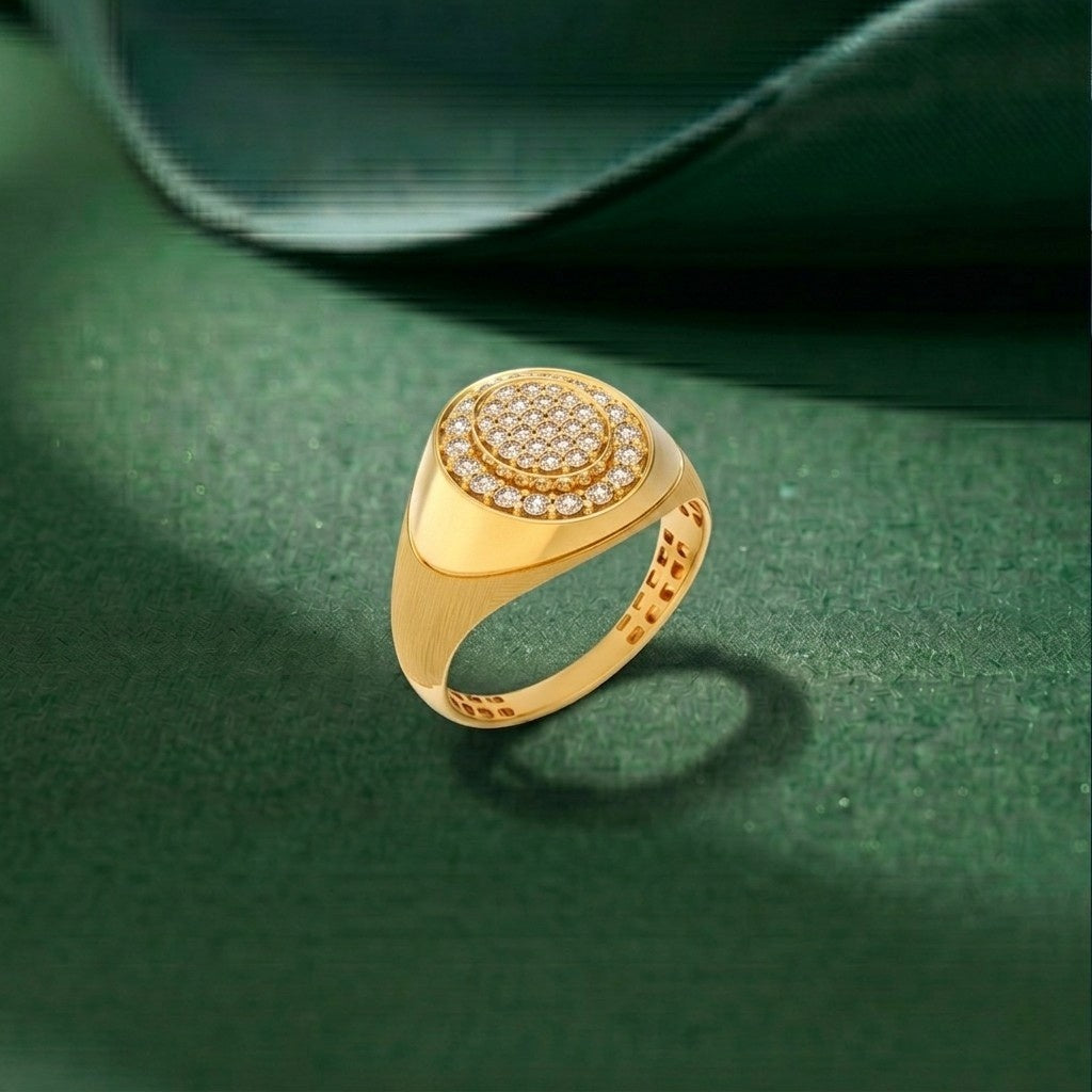 A gold signet ring with a circular pavé diamond center, displayed on a textured dark green surface.