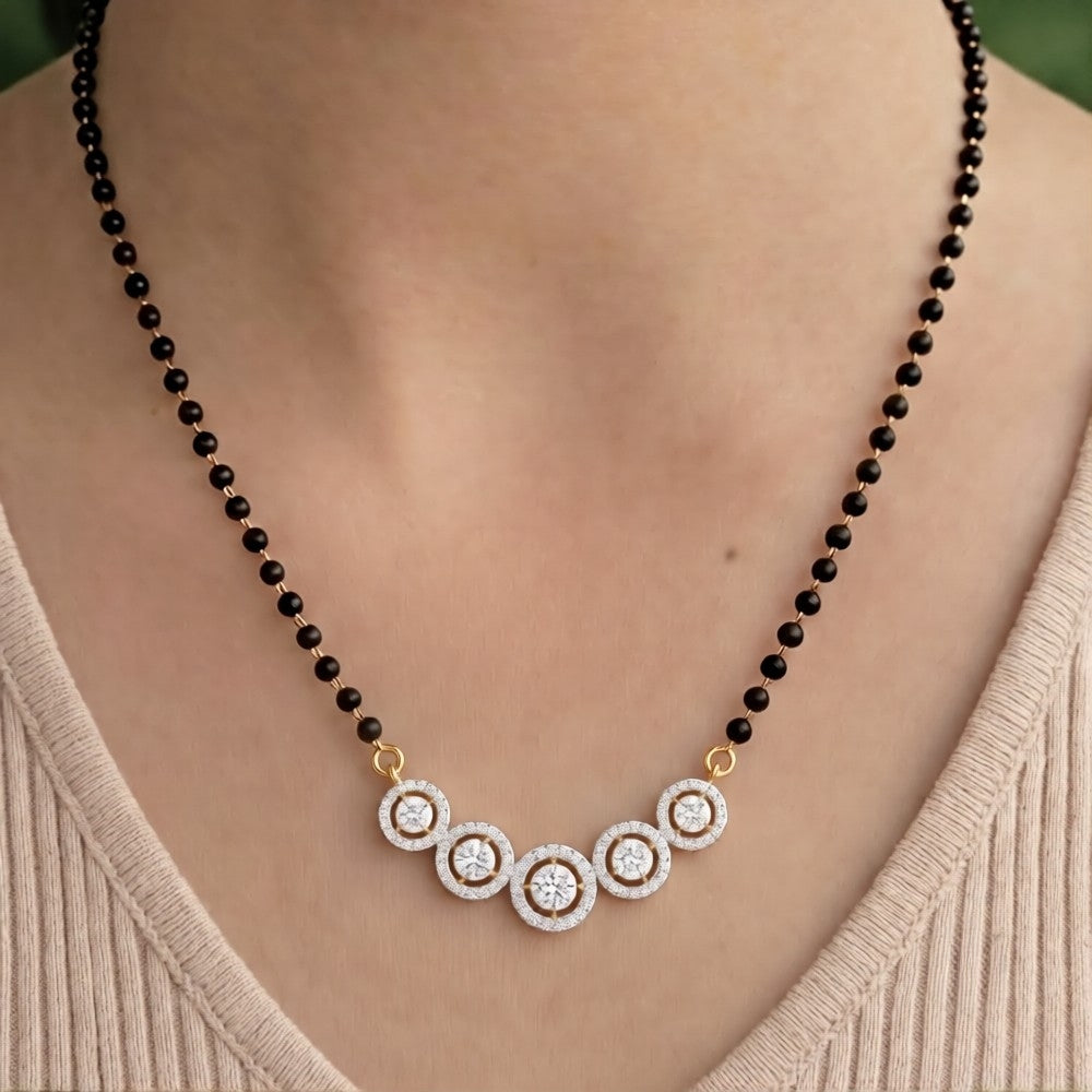 A gold chain magalsutra with five circular pavé diamond clusters connected by small black beads, displayed on  person neck.