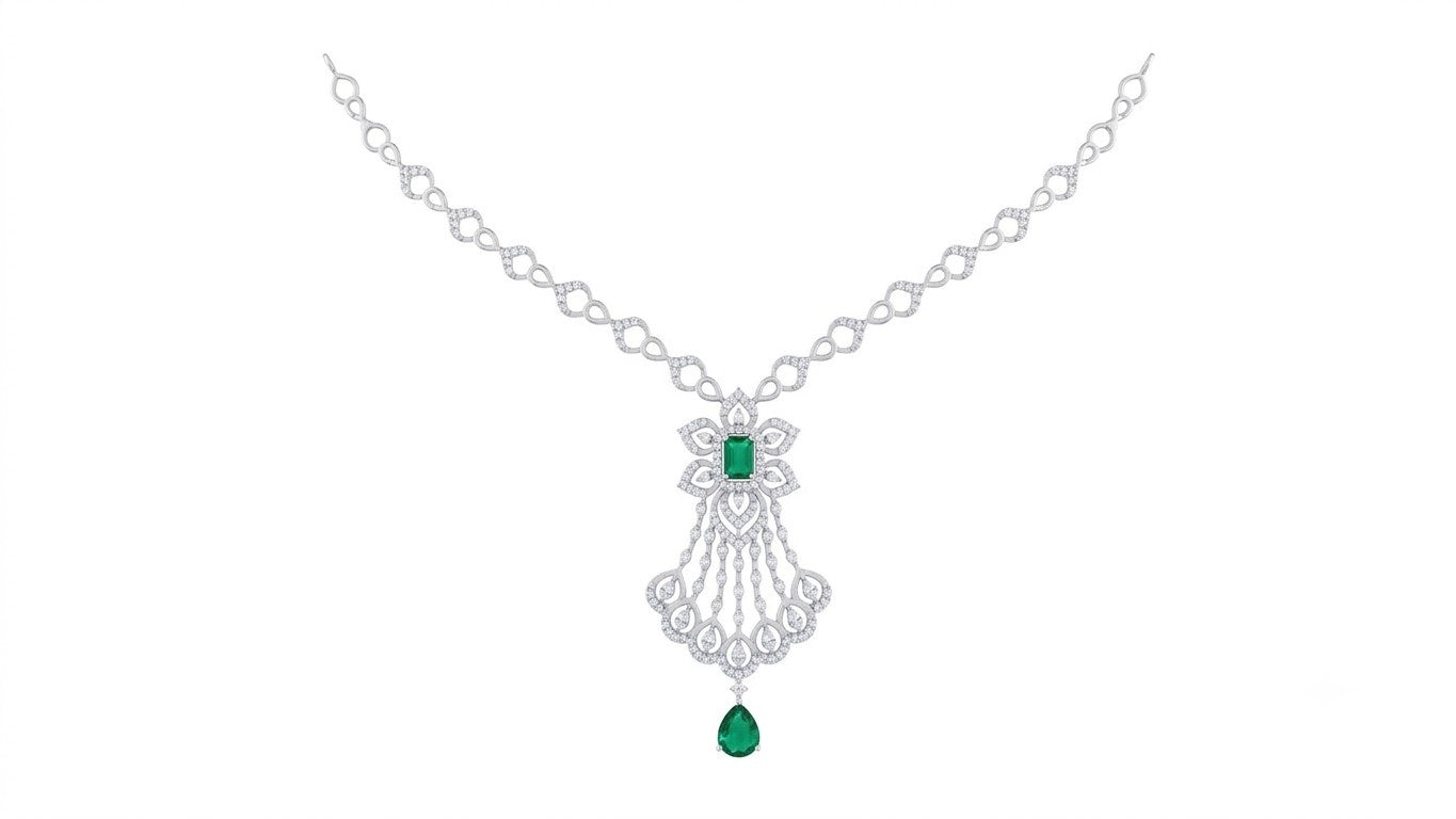 A white gold and diamond necklace with a central floral design featuring green emerald-cut gemstones shown on a plain white background.