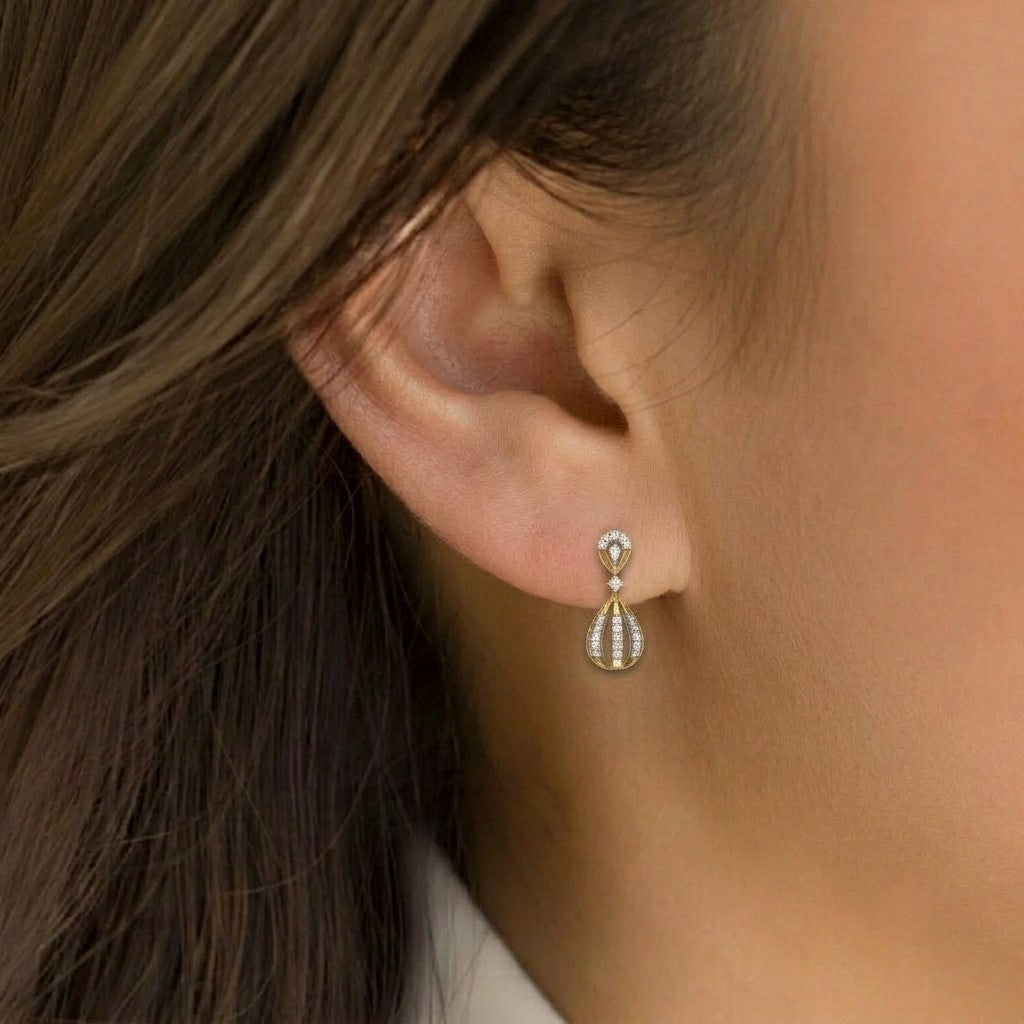 A close-up of a woman's ear wearing a small gold and white stone drop stud earring.