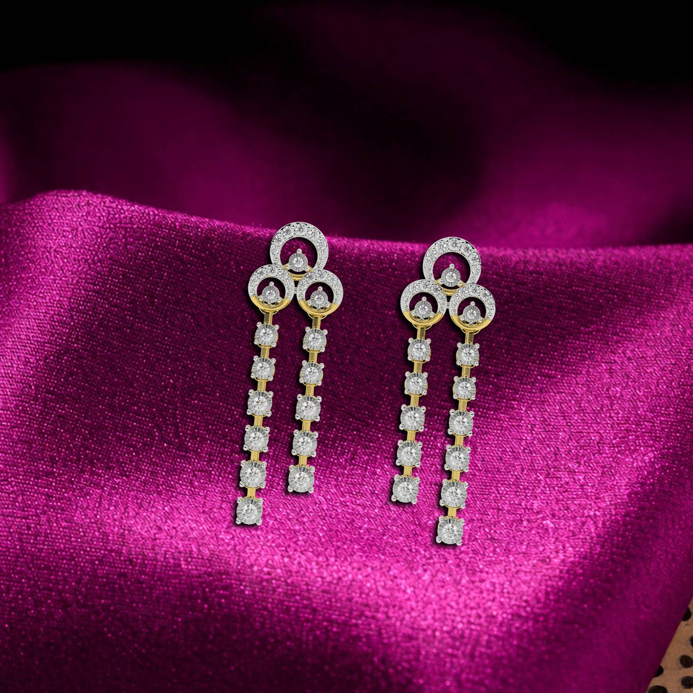 Gold earrings with multiple diamond accents along the length of each earring, featuring a timeless design on a magenta fabric background.
