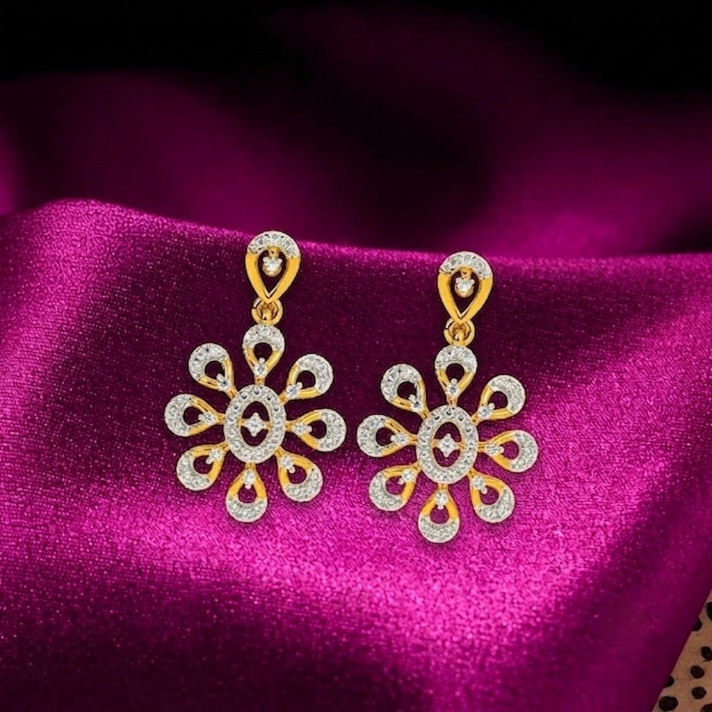 A pair of gold and diamond floral dangle earrings, displayed on a draped magenta satin fabric.
