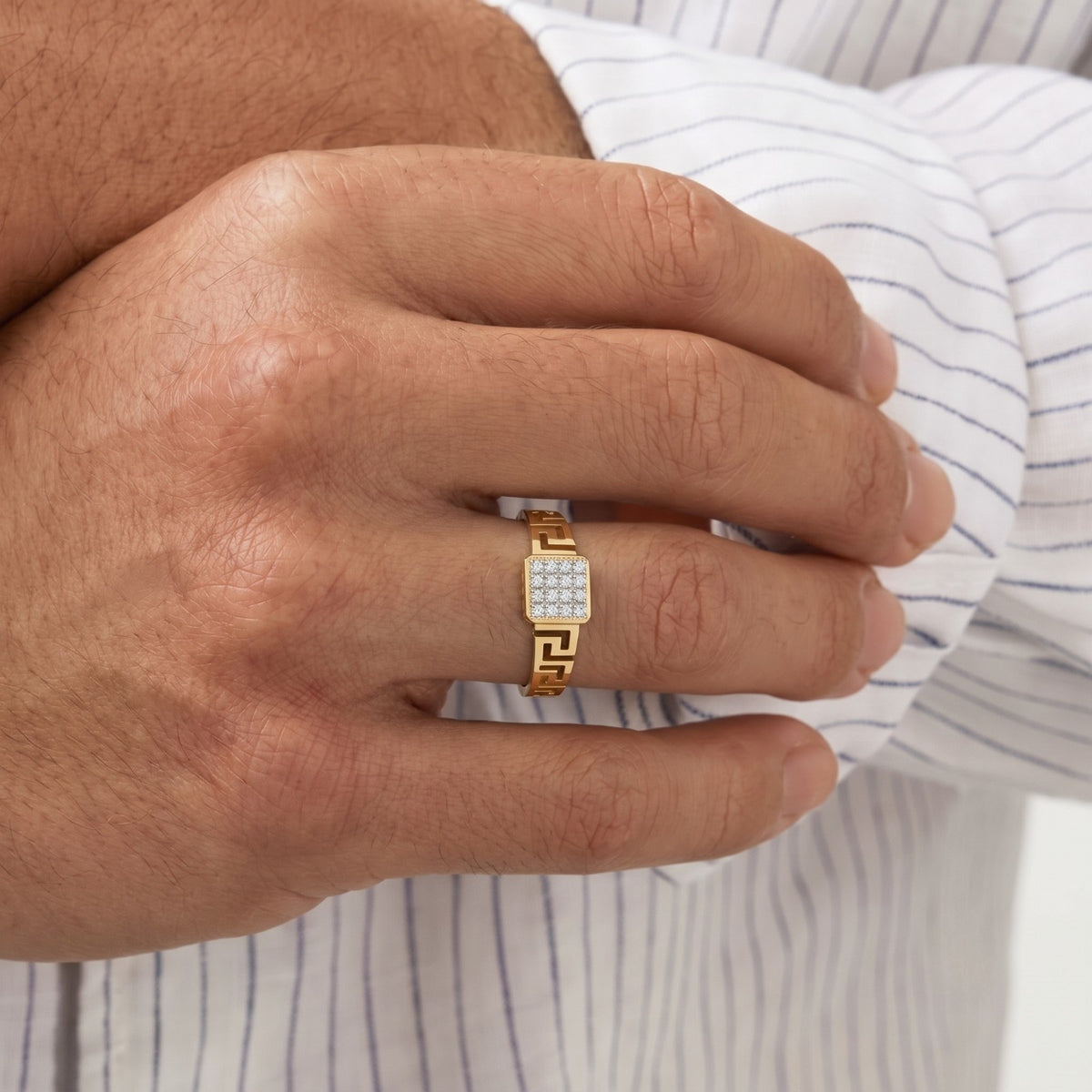Hand wearing a gold ring with a diamond on a striped shirt background.