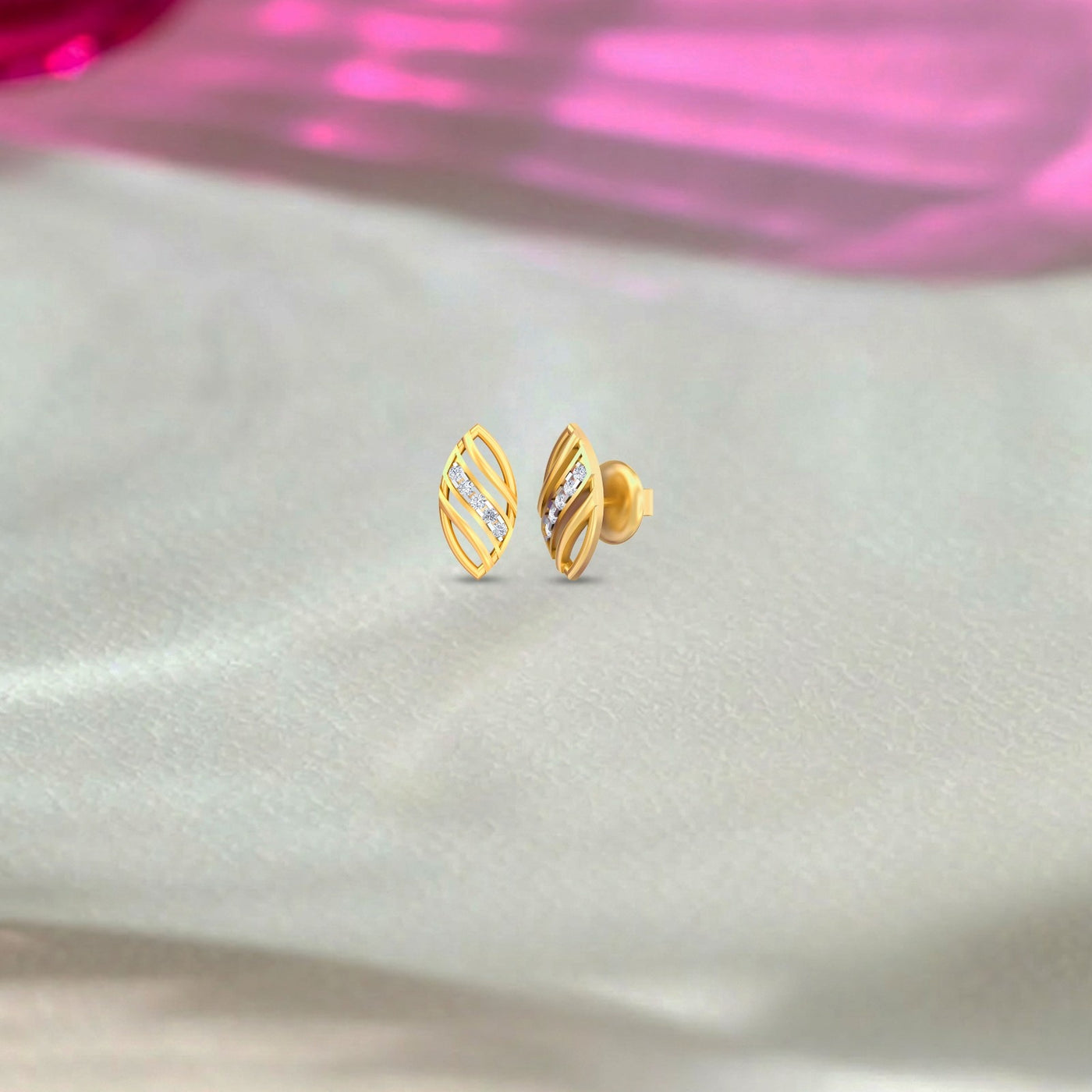 Yellow gold and diamond stud earrings on a fabric background.