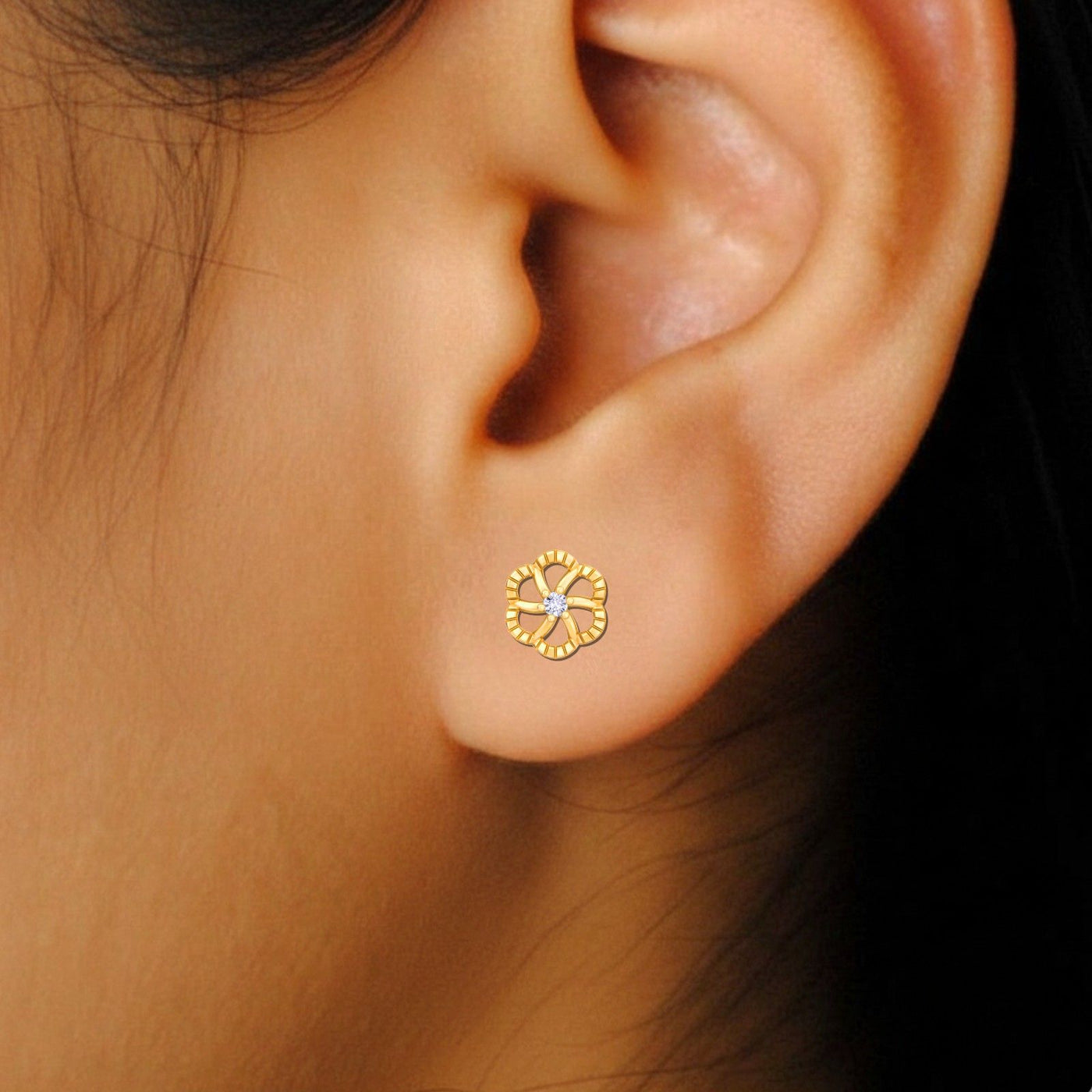 Close-up of an ear wearing a gold earring with a central diamond.