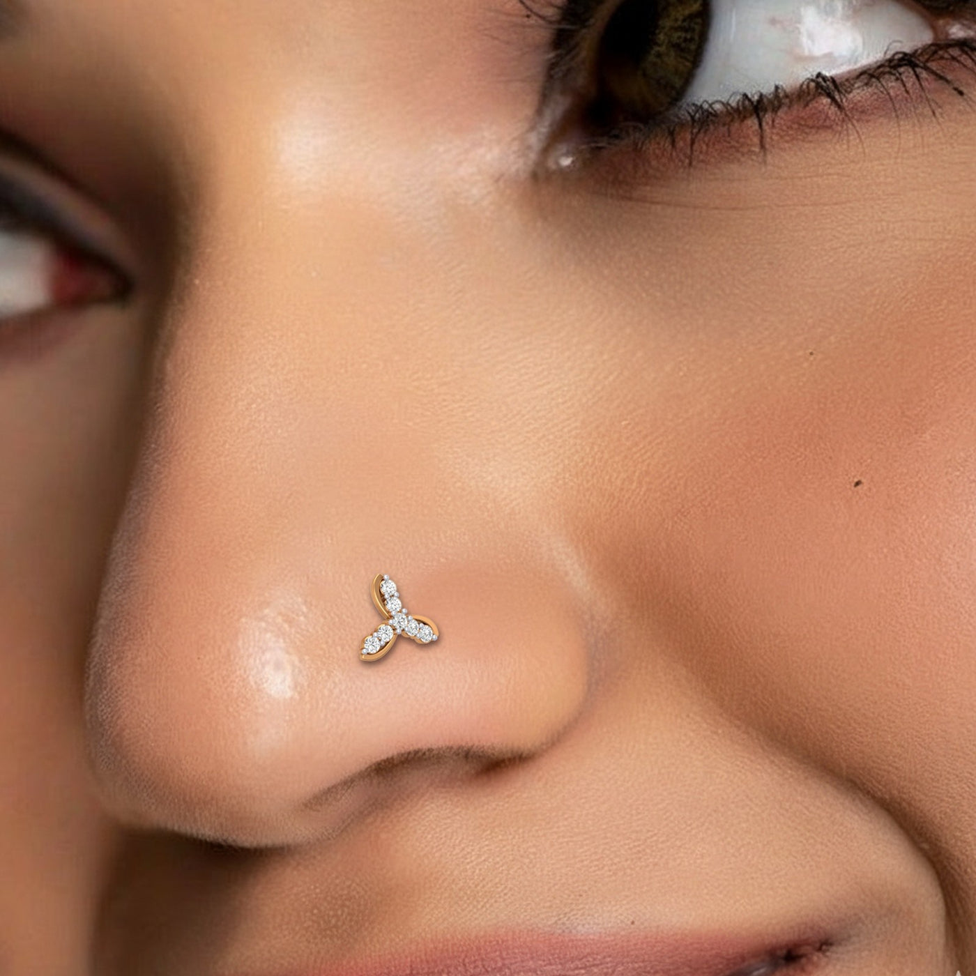 Extreme close-up of a person's face highlighting a delicate gold nose stud with a three-petaled, trefoil-like design encrusted with small diamonds on the nostril