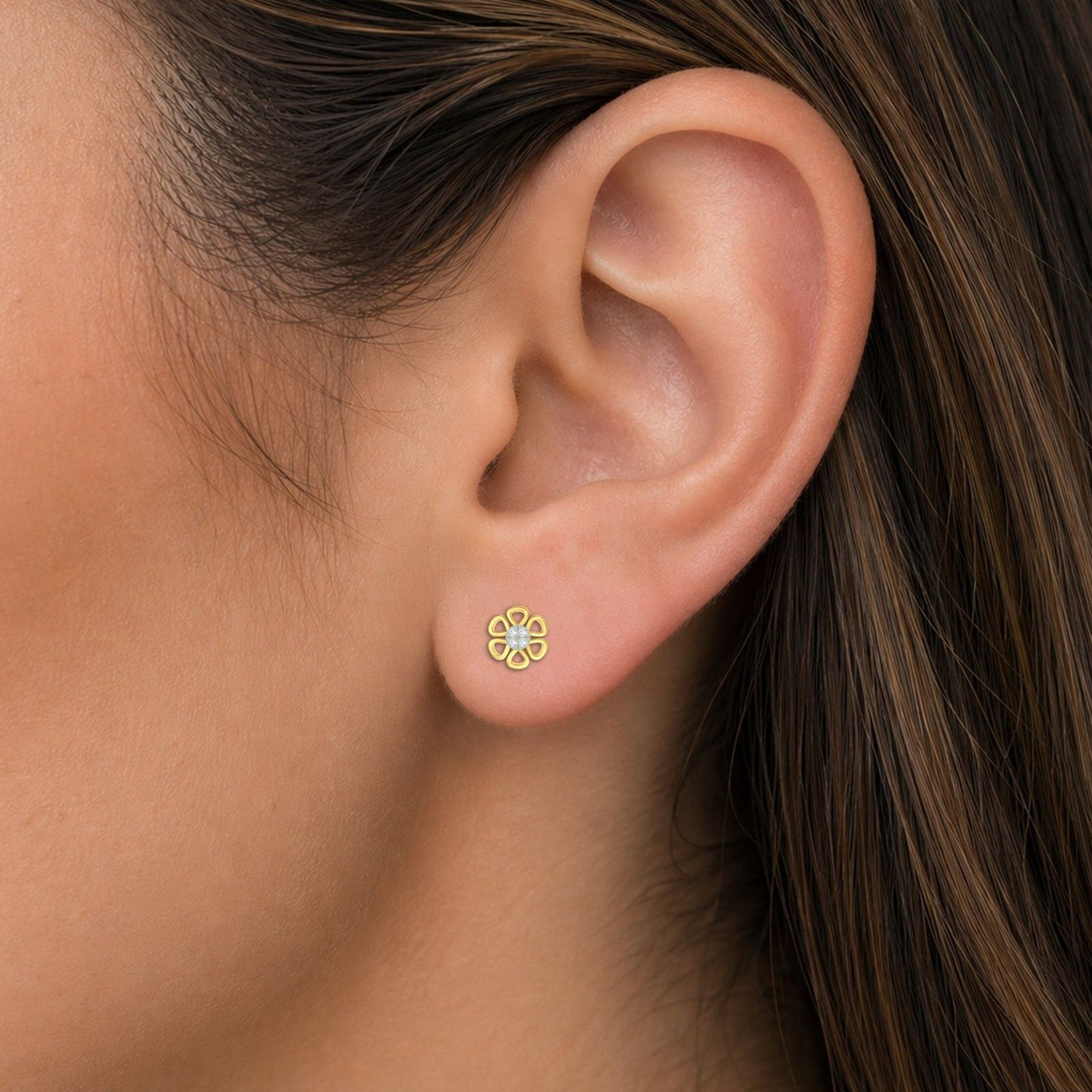 A close-up of a woman's ear wearing a small, flower-shaped yellow gold stud earring with a central diamond.