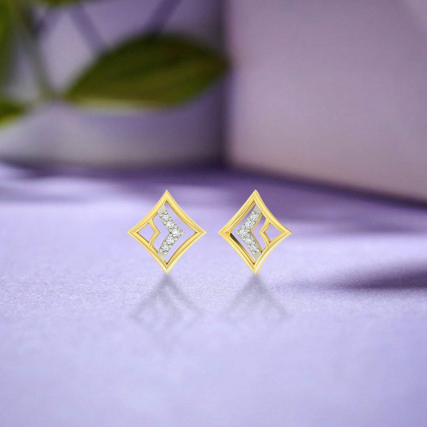 A pair of geometric yellow gold and diamond stud earrings resting on a soft lavender surface with subtle reflections