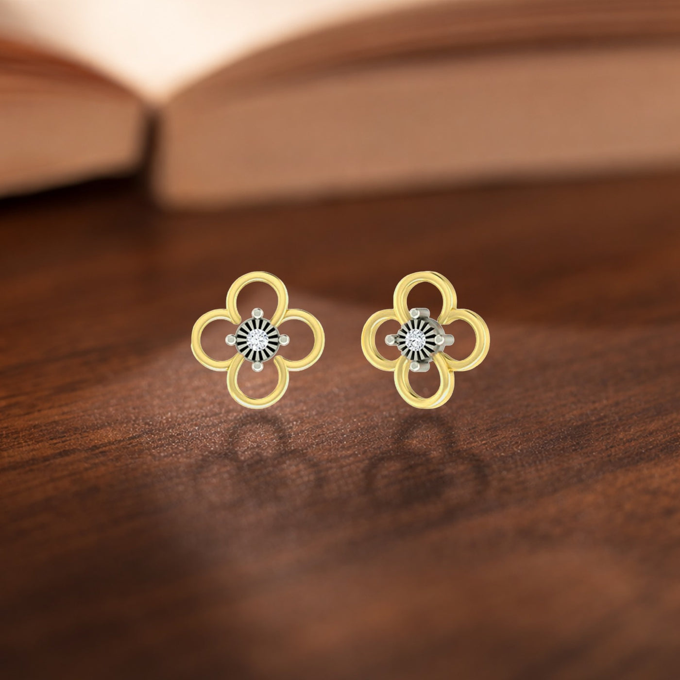 A pair of yellow gold openwork clover stud earrings with diamond centers on a wooden surface