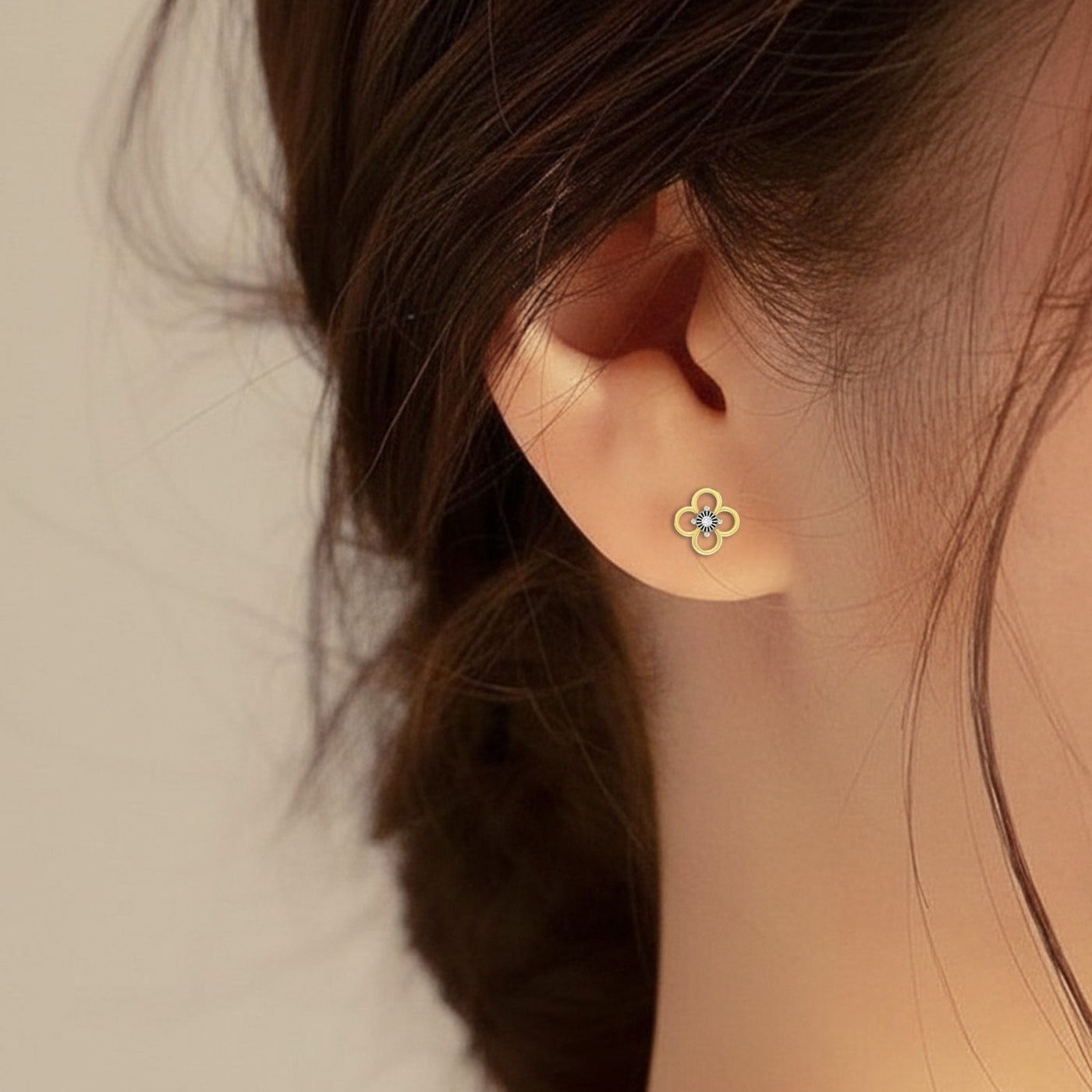 A close-up of a person wearing a delicate gold clover-shaped stud earring
