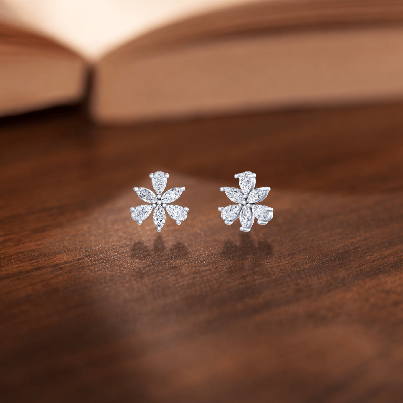 Gold and diamond flower-shaped earrings on a wooden background surface.