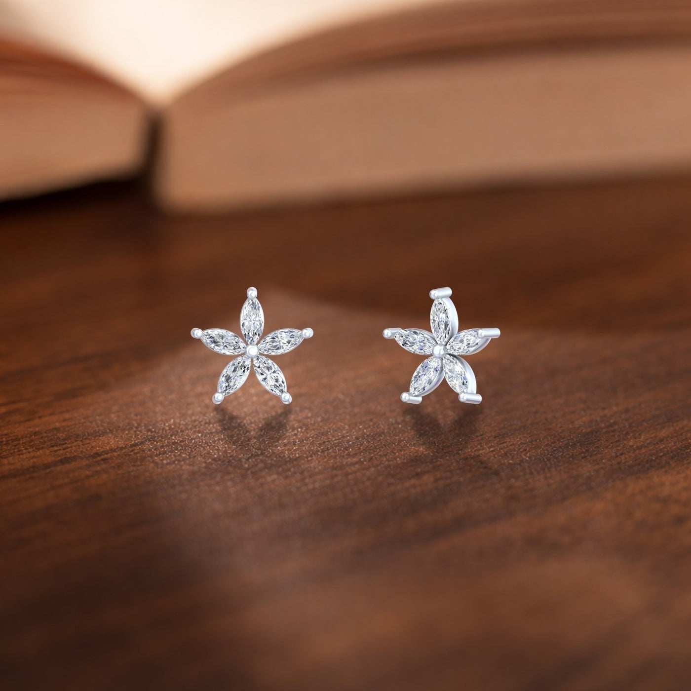 Gold flower-shaped stud earrings with marquise-cut diamond, shown on a wooden surface.