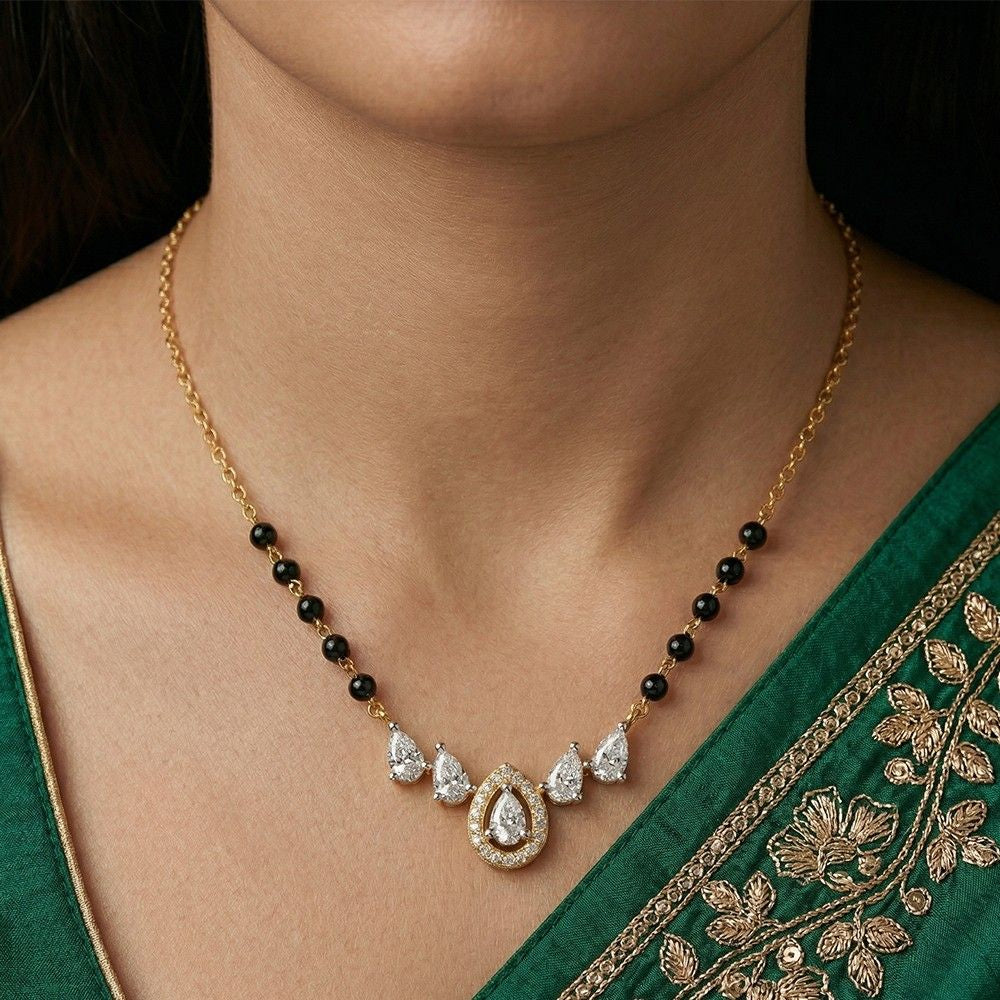 Gold and diamond mangalsutra with black beads and teardrop-shaped diamonds on a person wearing a green saree.