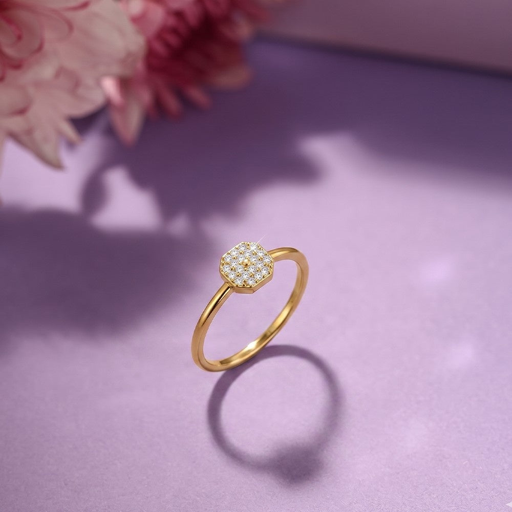 Gold ring with a diamond-like center on a purple surface with pink flowers.