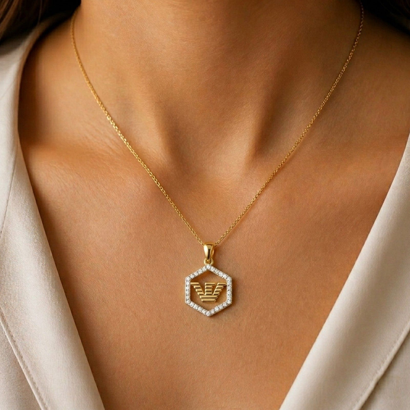 Gold necklace with a hexagonal pendant featuring an eagle emblem on a person wearing a beige outfit.
