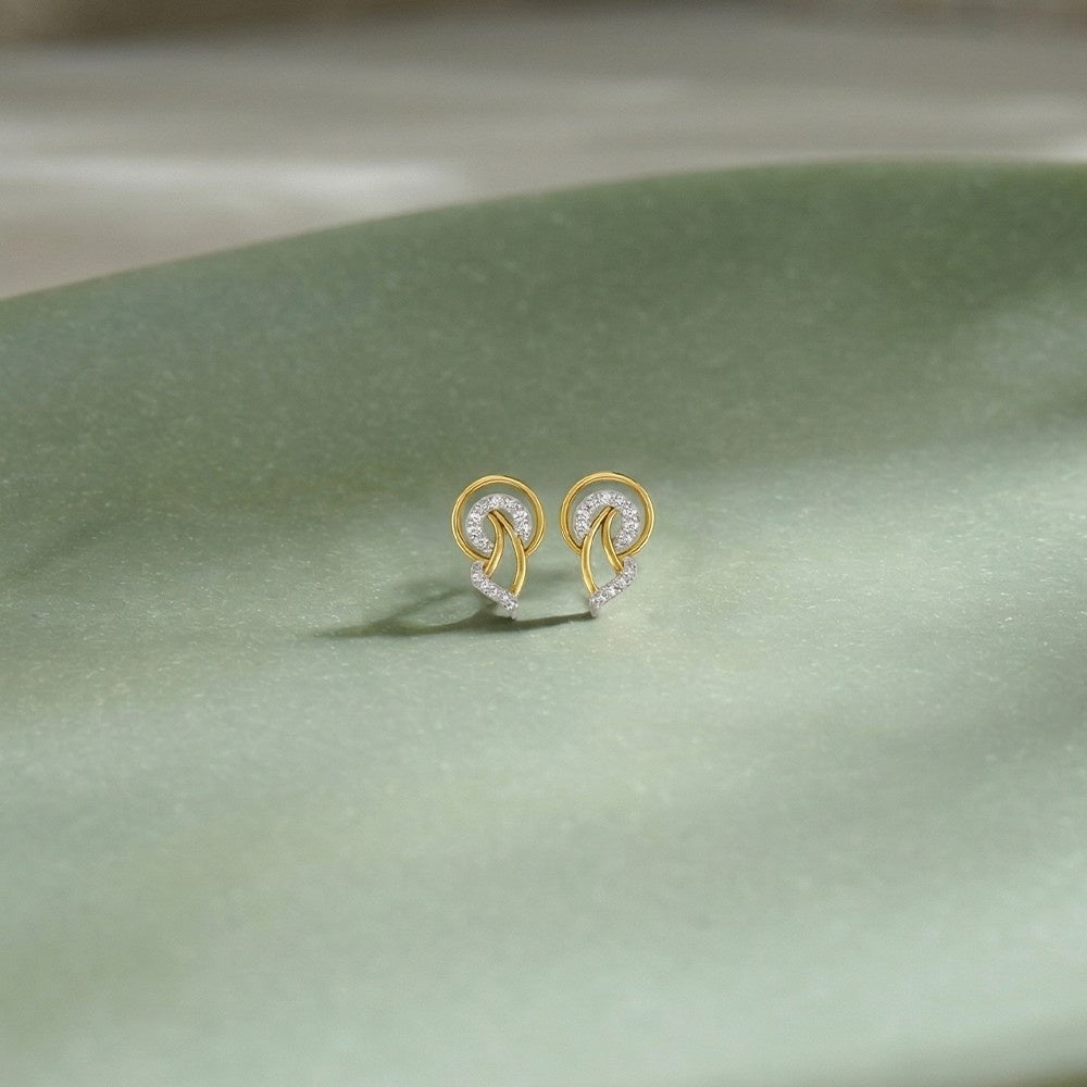 Gold and diamond stud earrings on a light green background.