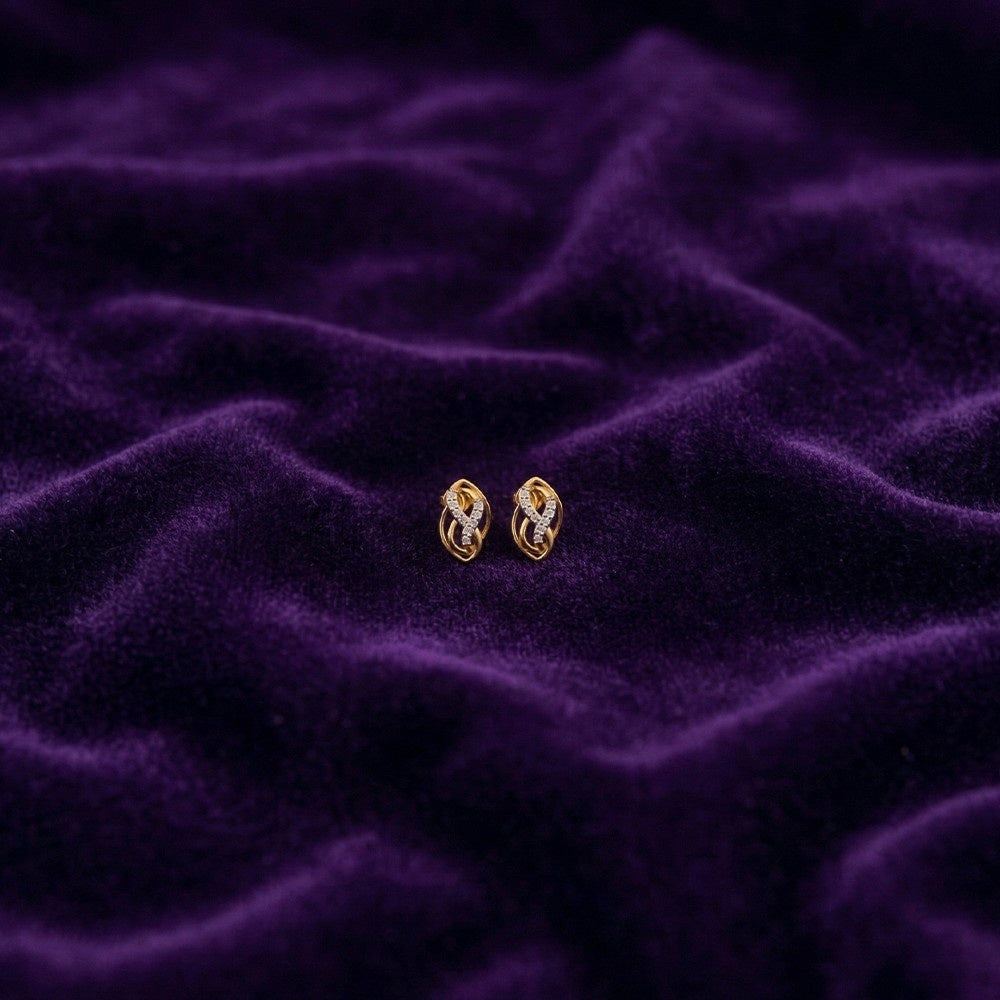 Gold and diamond stud earrings on a purple textured fabric background.