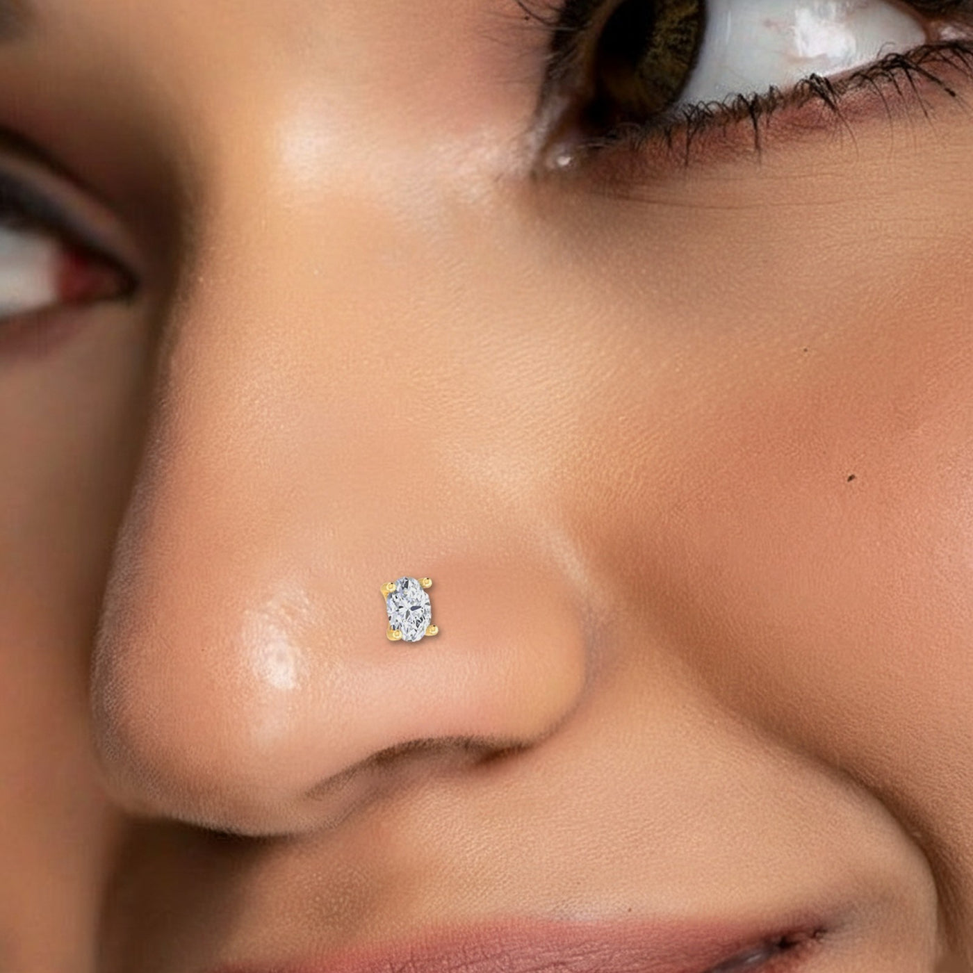 A close-up of a person's nose wearing a small nose stud earring with a clear faceted gemstone and gold-toned setting.