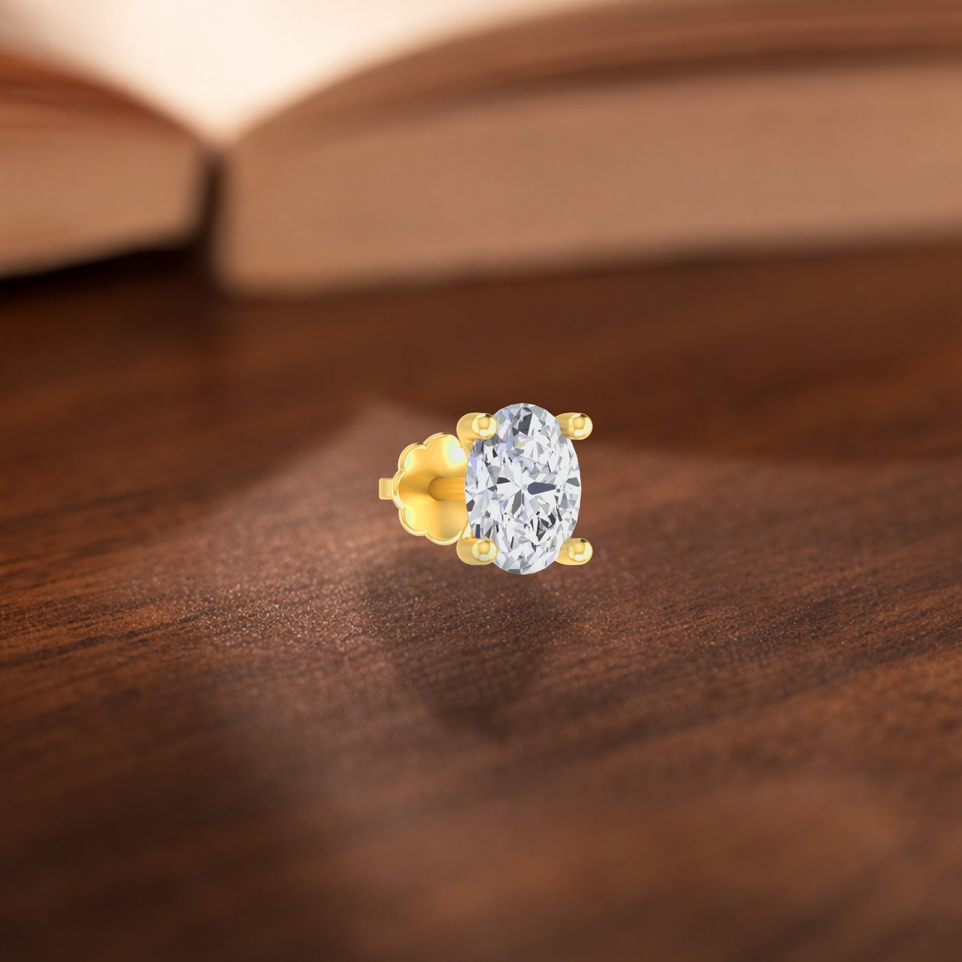 A close-up of a single gold stud nose pin featuring an oval-cut clear gemstone in a four-prong setting