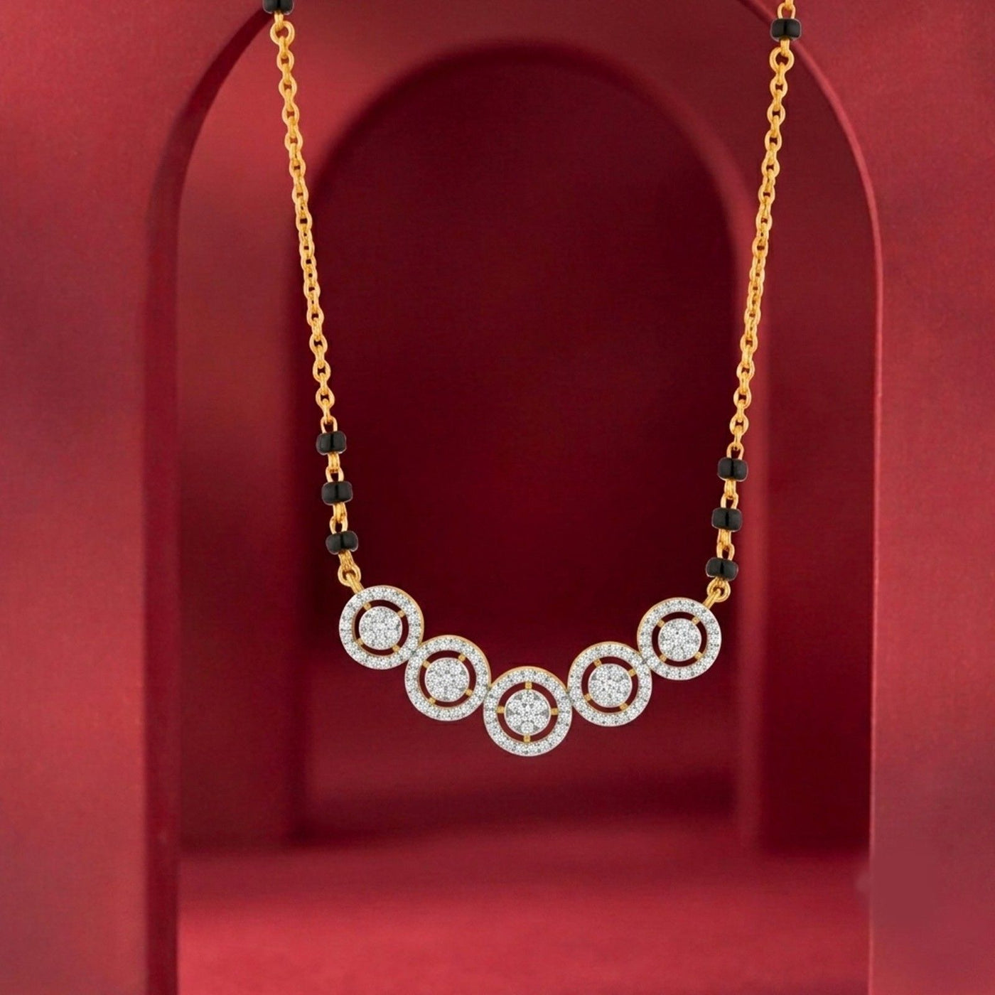 A gold chain magalsutra with five circular pavé diamond clusters connected by small black beads, displayed against a red arched backdrop.