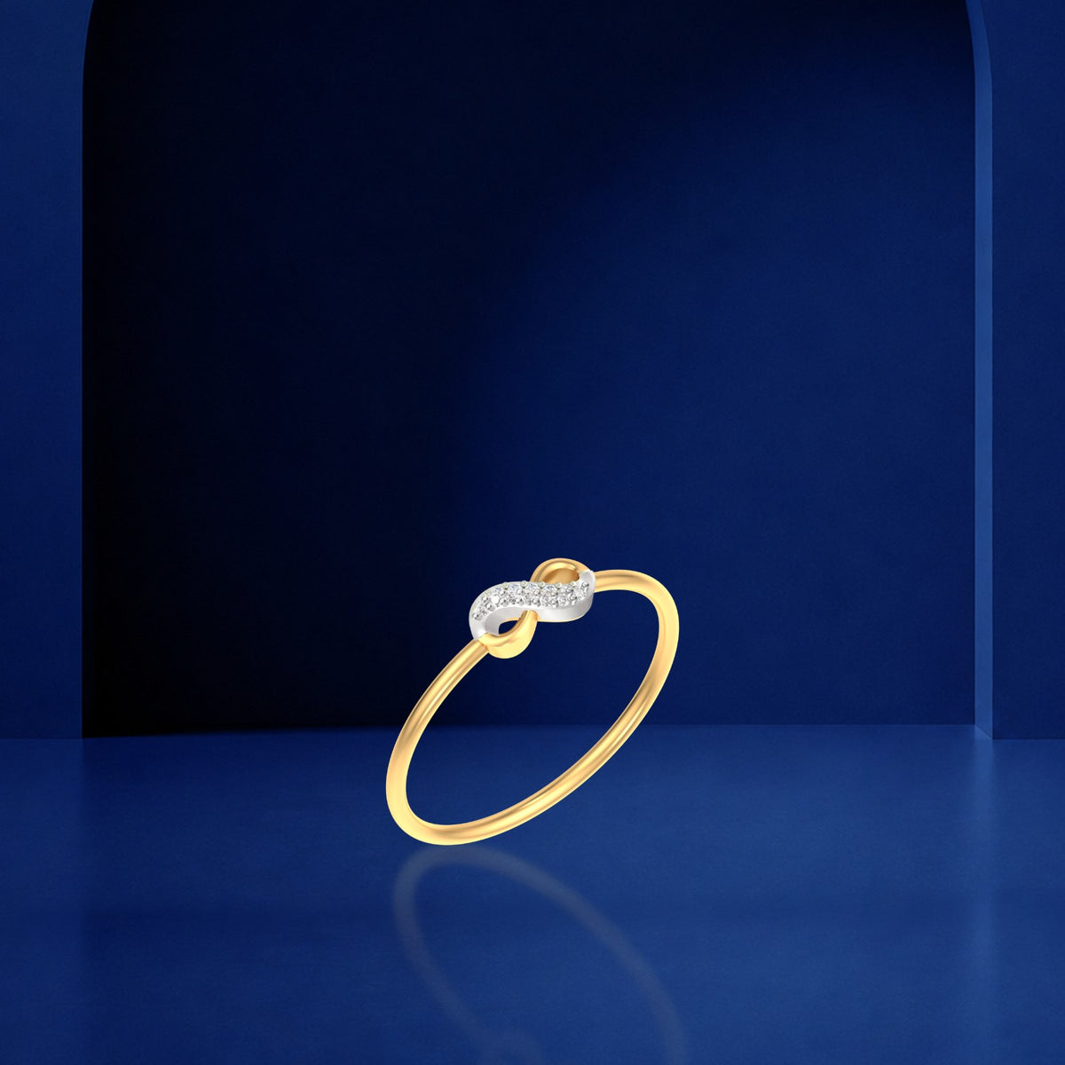 A gold ring with a diamond-encrusted infinity symbol at the top, displayed on a dark blue reflective surface.