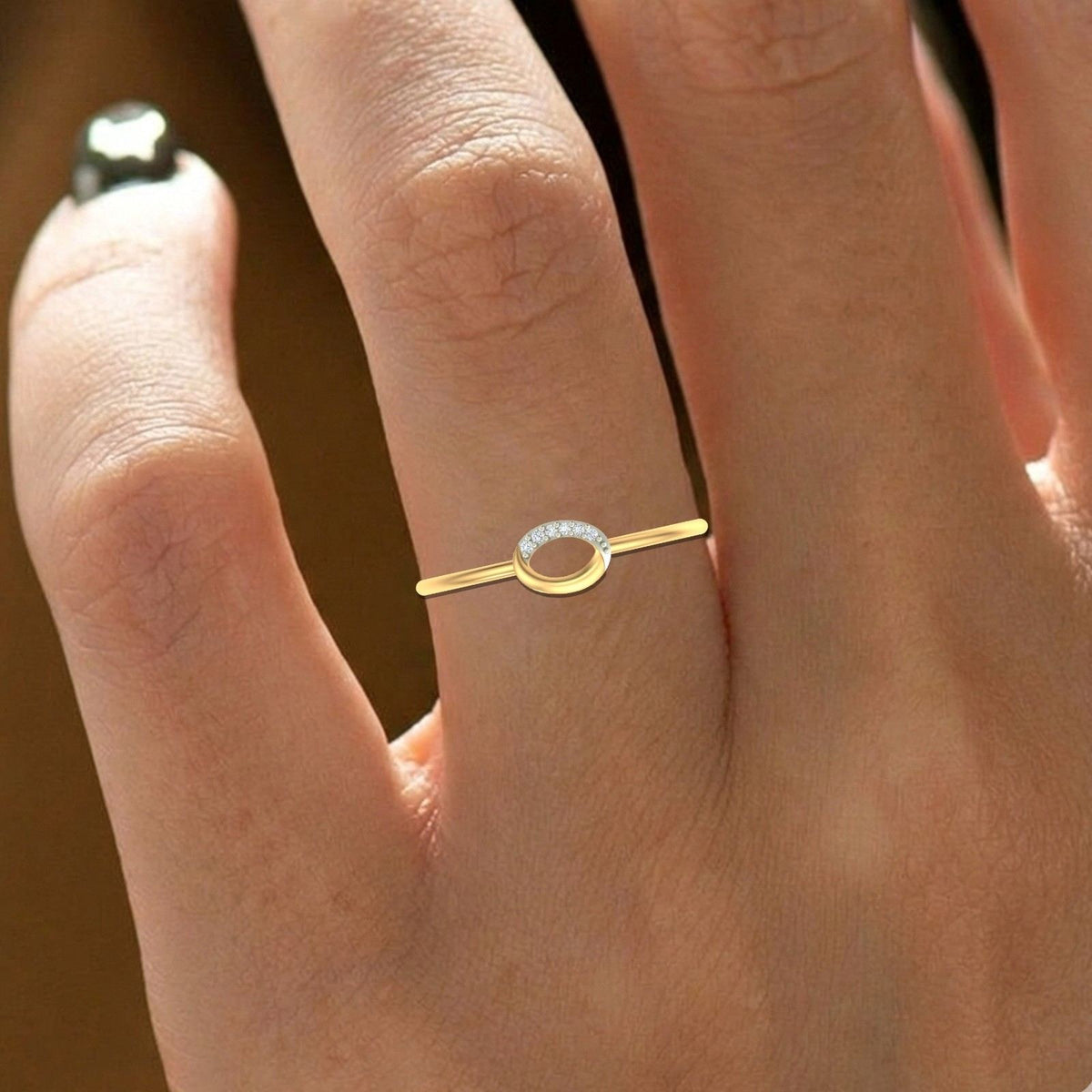 Gold ring with a small diamond on a person's finger against a blurred background