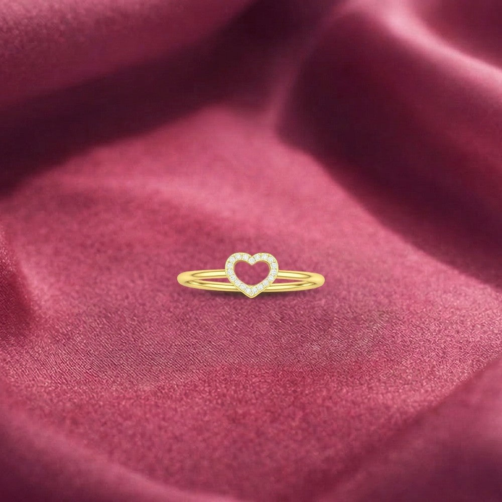 A delicate yellow gold ring featuring a heart-shaped, resting on a draped, textured dusty rose velvet fabric.