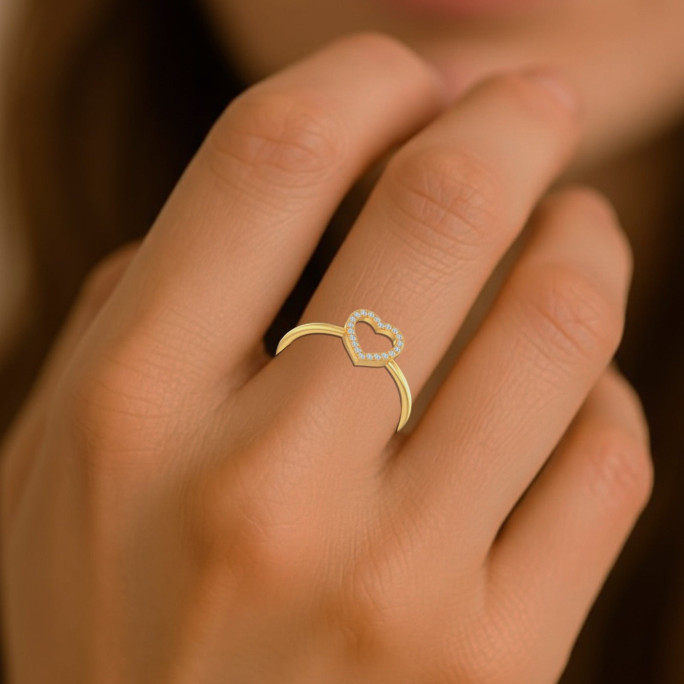 Gold ring with a heart design on a person's finger against a blurred background