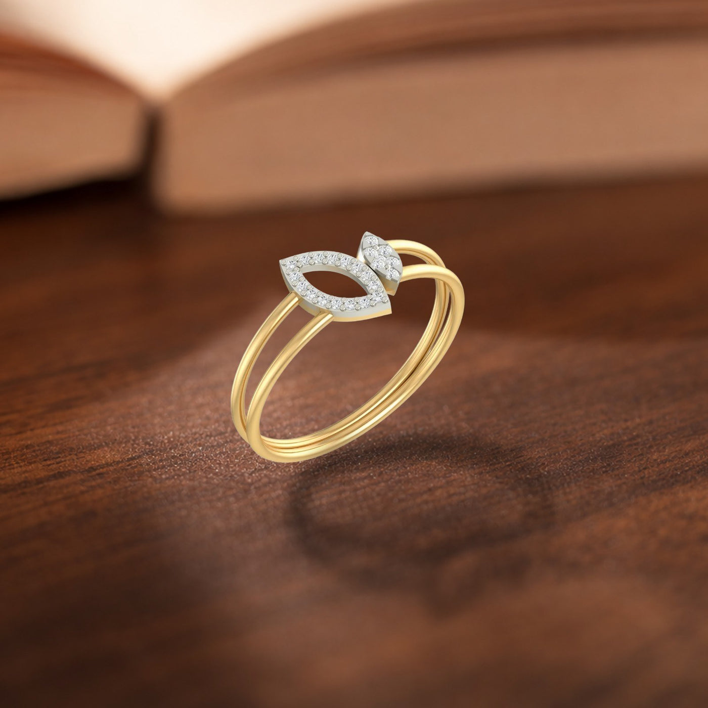 A gold ring with a diamond-encrusted leaf-shaped top, resting on a polished wooden surface.