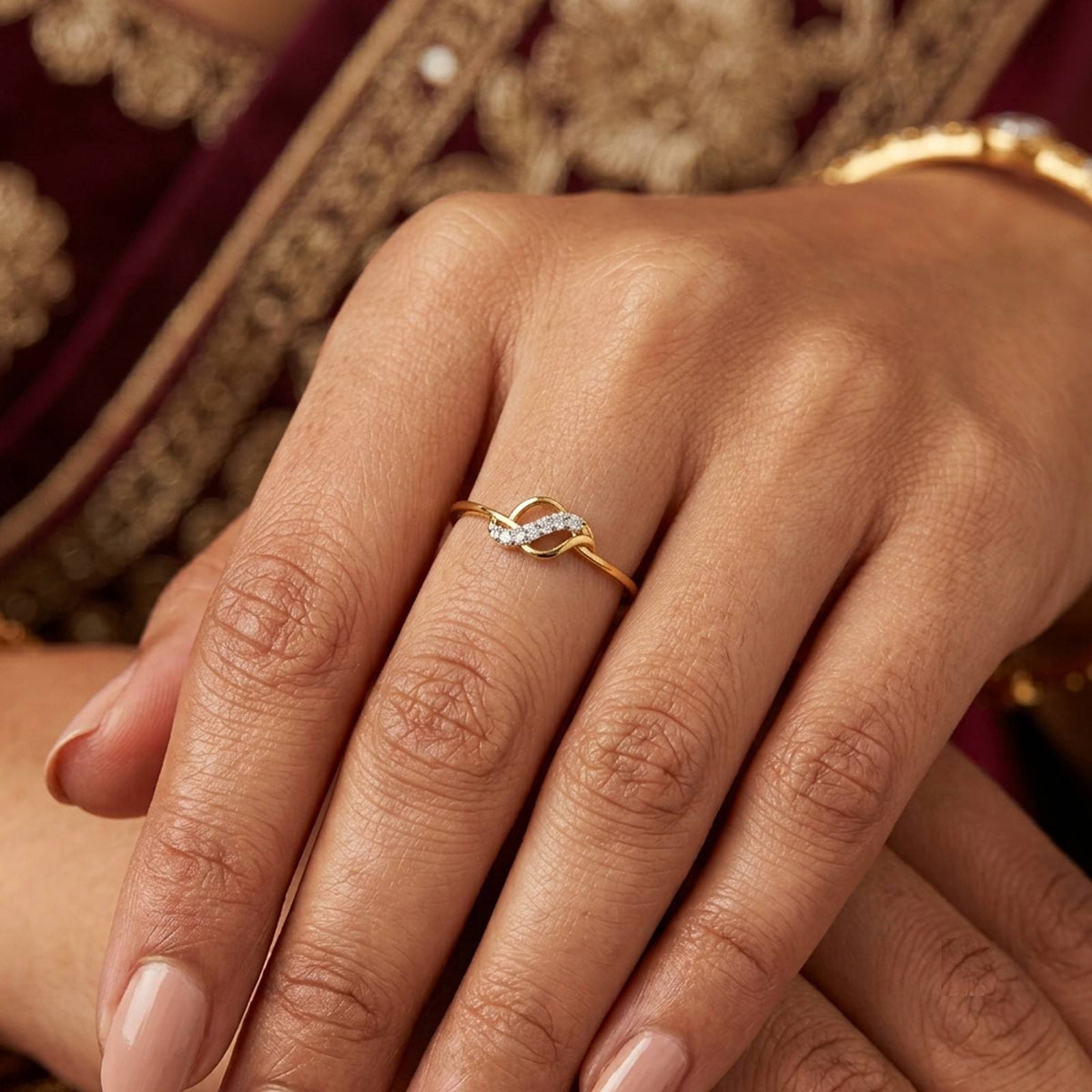 A gold and diamond ring with a deep maroon and gold embroidered traditional garment visible in the background.