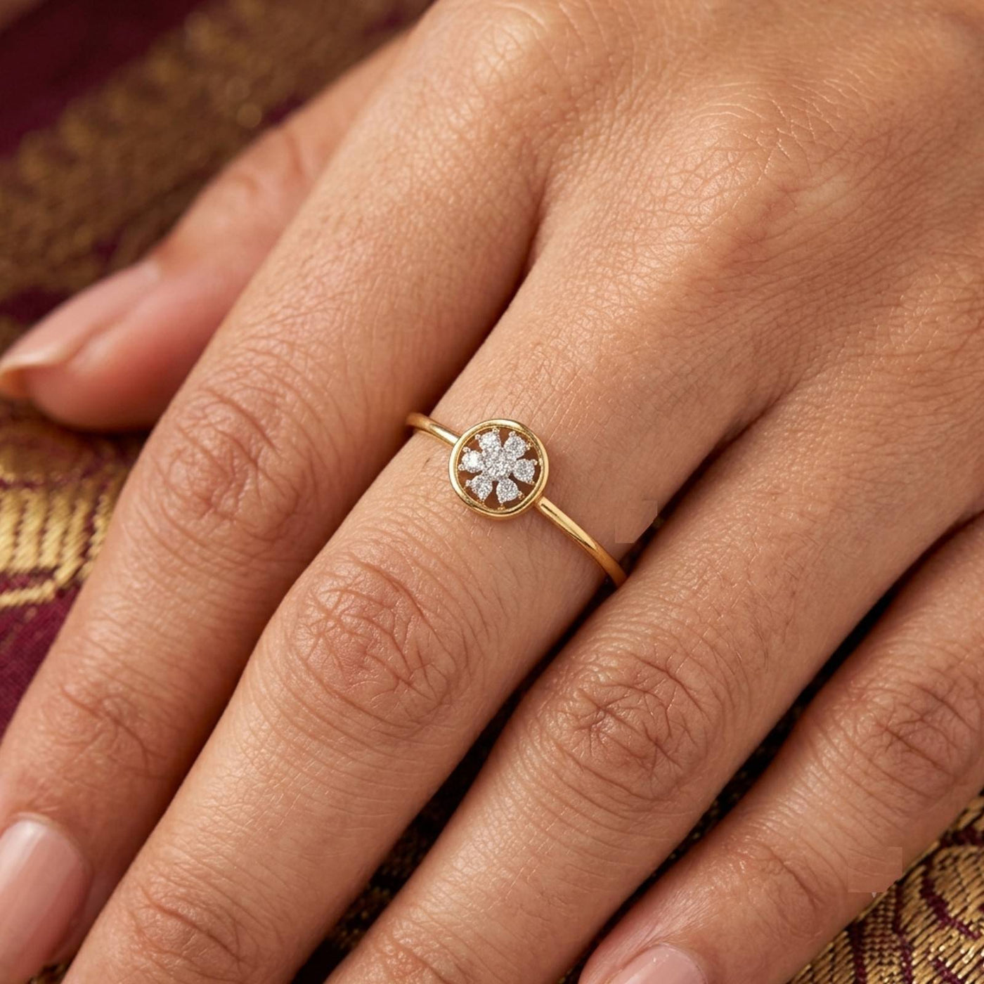 A close-up of a hand wearing a delicate gold ring with a small flower-shaped diamond cluster ring.
