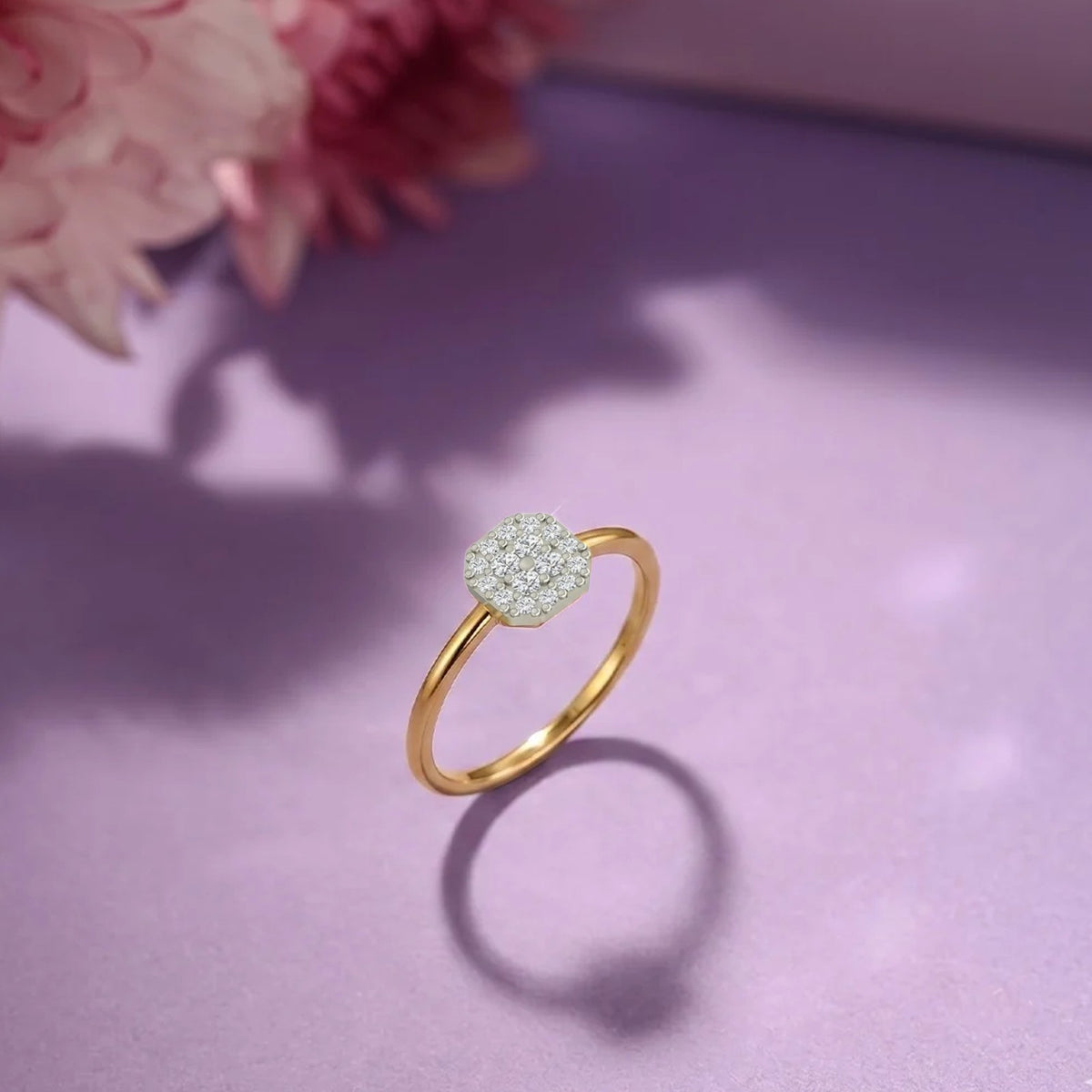 A gold and diamond ring with a round cluster, displayed on a soft lavender surface with a blurred pink flower in the background.