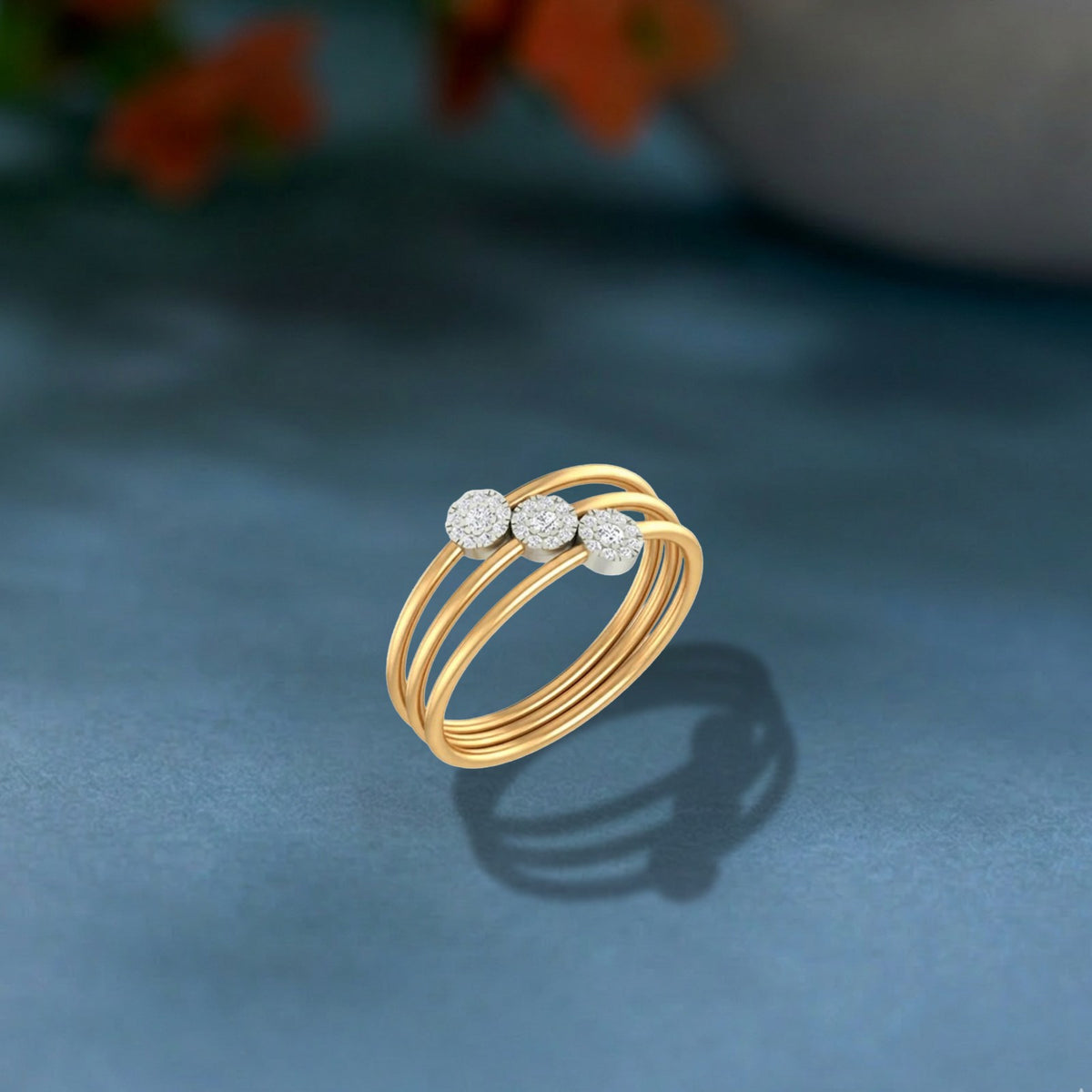 A gold ring with three parallel bands and three small round diamonds, on a blue surface with a soft blurred background.