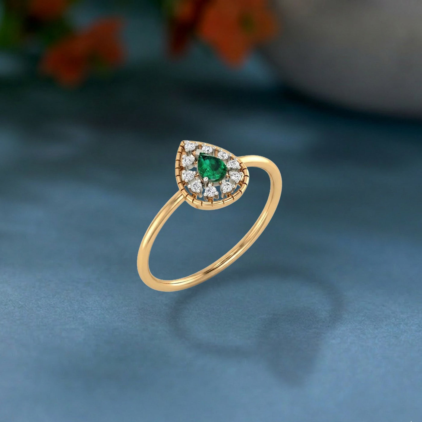 Gold and diamond with teardrop emerald gemstone setting on a teal surface.