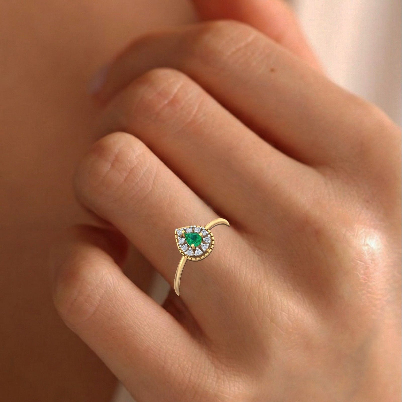 Gold and diamond with teardrop emerald gemstone setting on a person's finger.