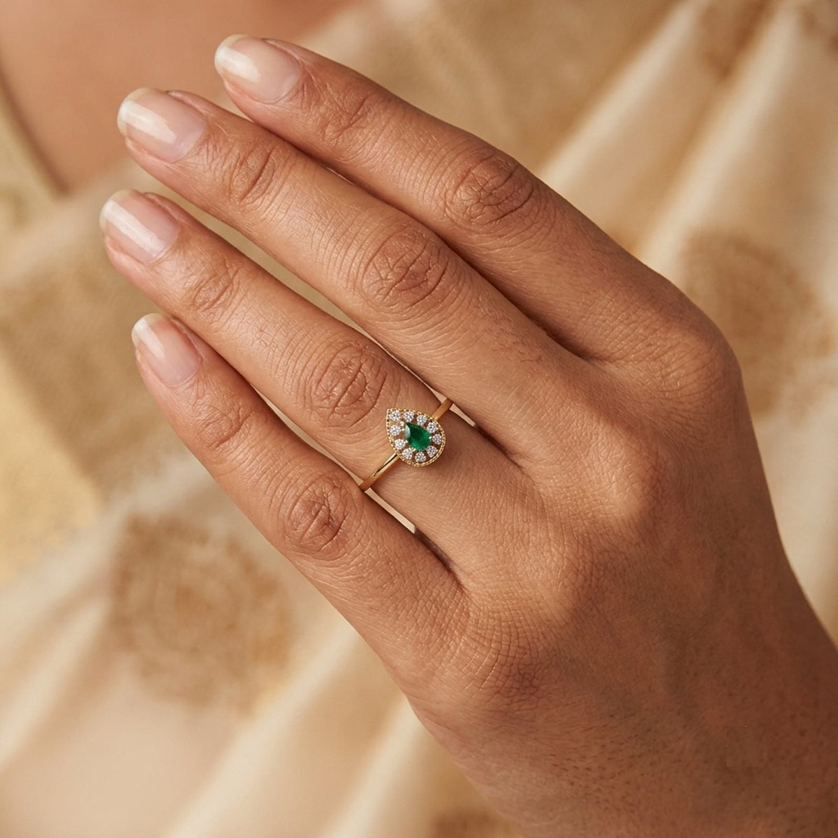 Gold and diamond with teardrop emerald gemstone setting on a person's finger.
