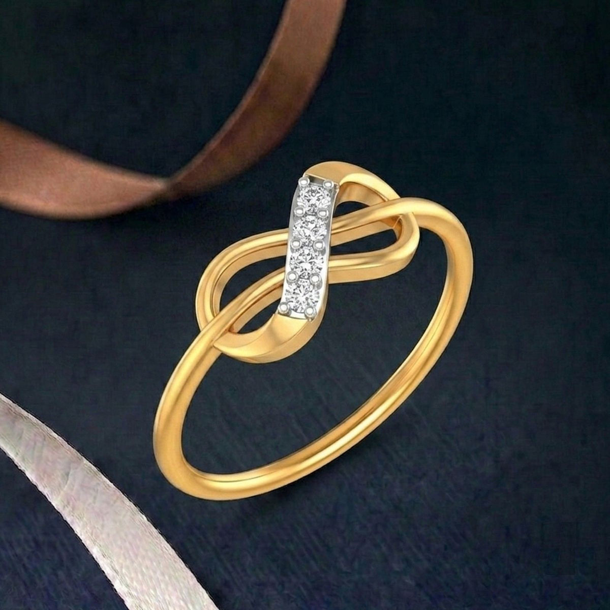 A gold ring with a double-loop infinity design and a central vertical ring on a dark textured background with ribbon props.