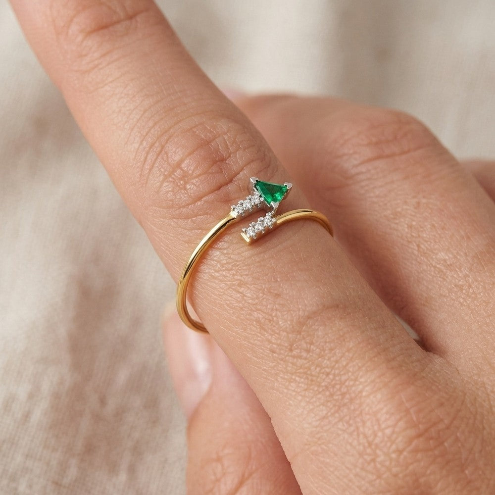 Gold ring with a emerald gemstone on a finger against a neutral background