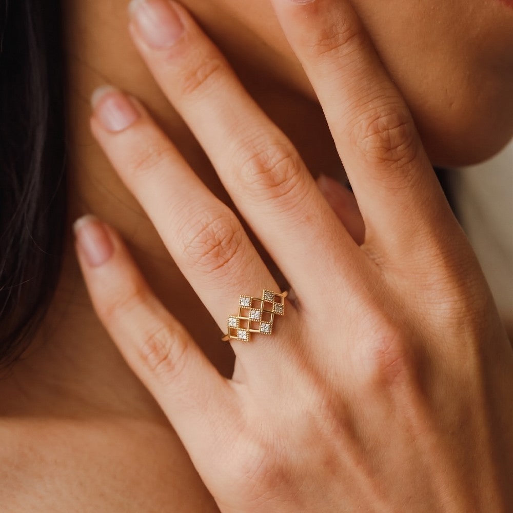 A close-up lifestyle shot of a person's hand wearing a gold ring with a geometric diamond pattern.