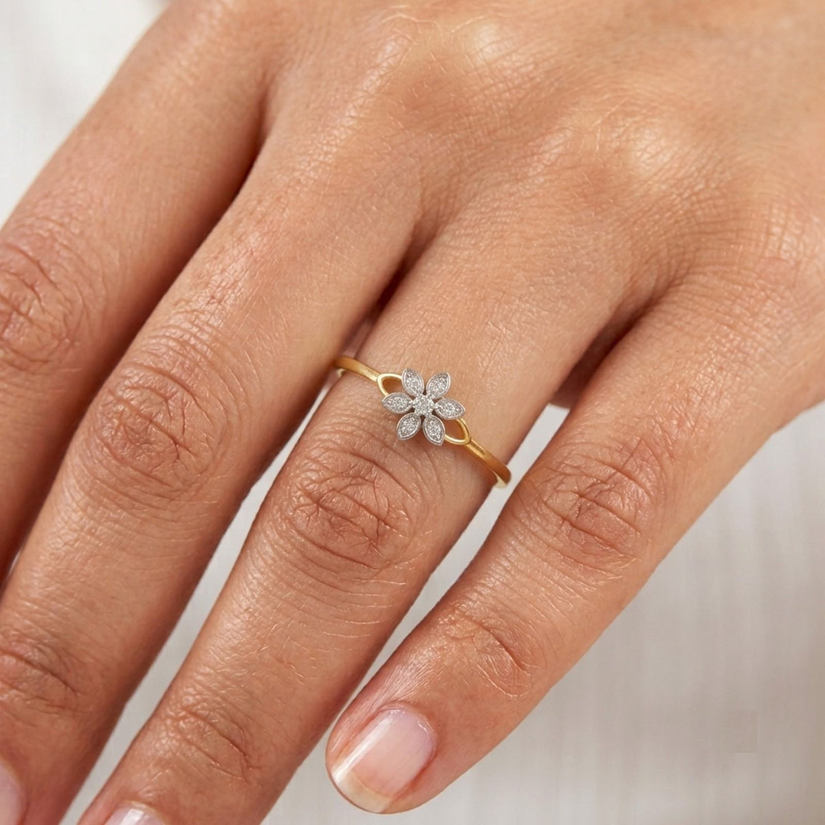 Gold and diamond ring with a floral design on a person's finger.