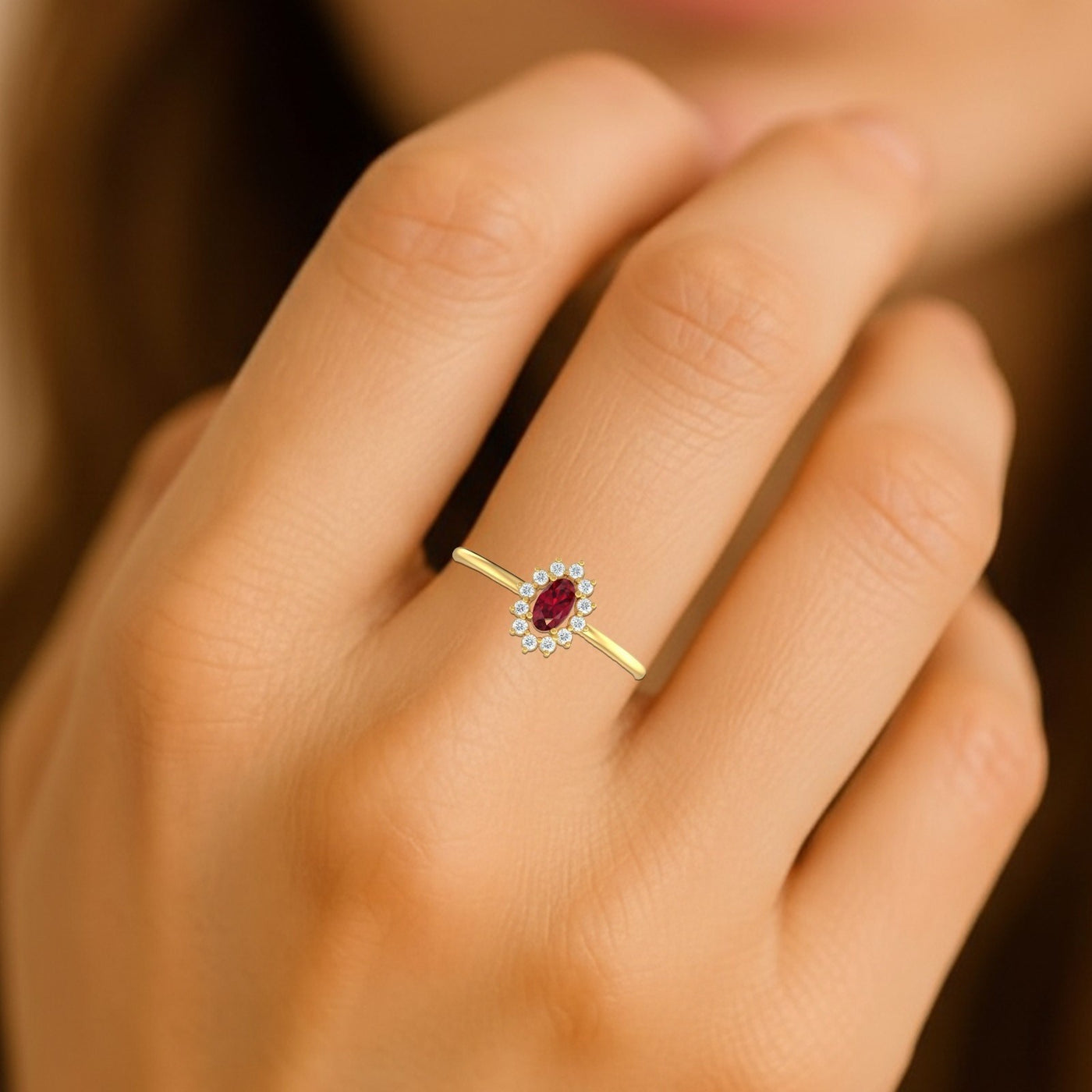 Gold and diamond with oval-shaped ruby gemstone setting on a person's finger.