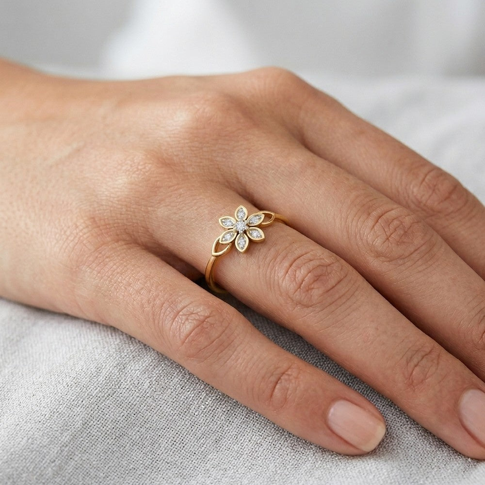 A close-up view of a person's hand wearing a yellow gold ring with a diamond-studded flower design