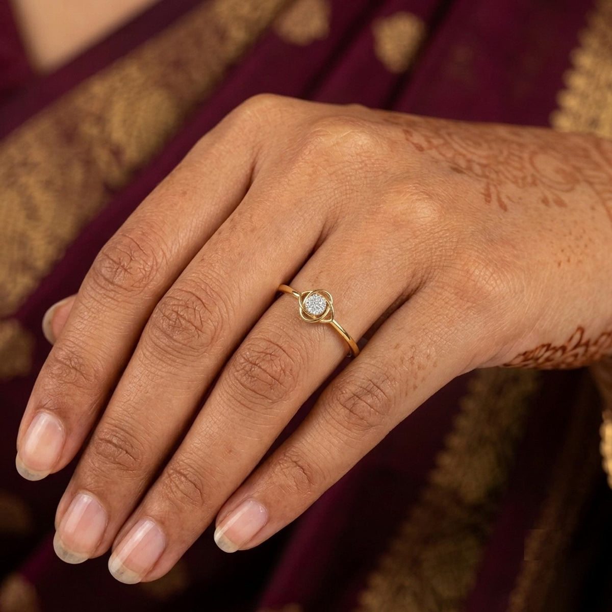 A close-up of a hand wearing a delicate gold ring, set against a dark purple and gold fabric background.